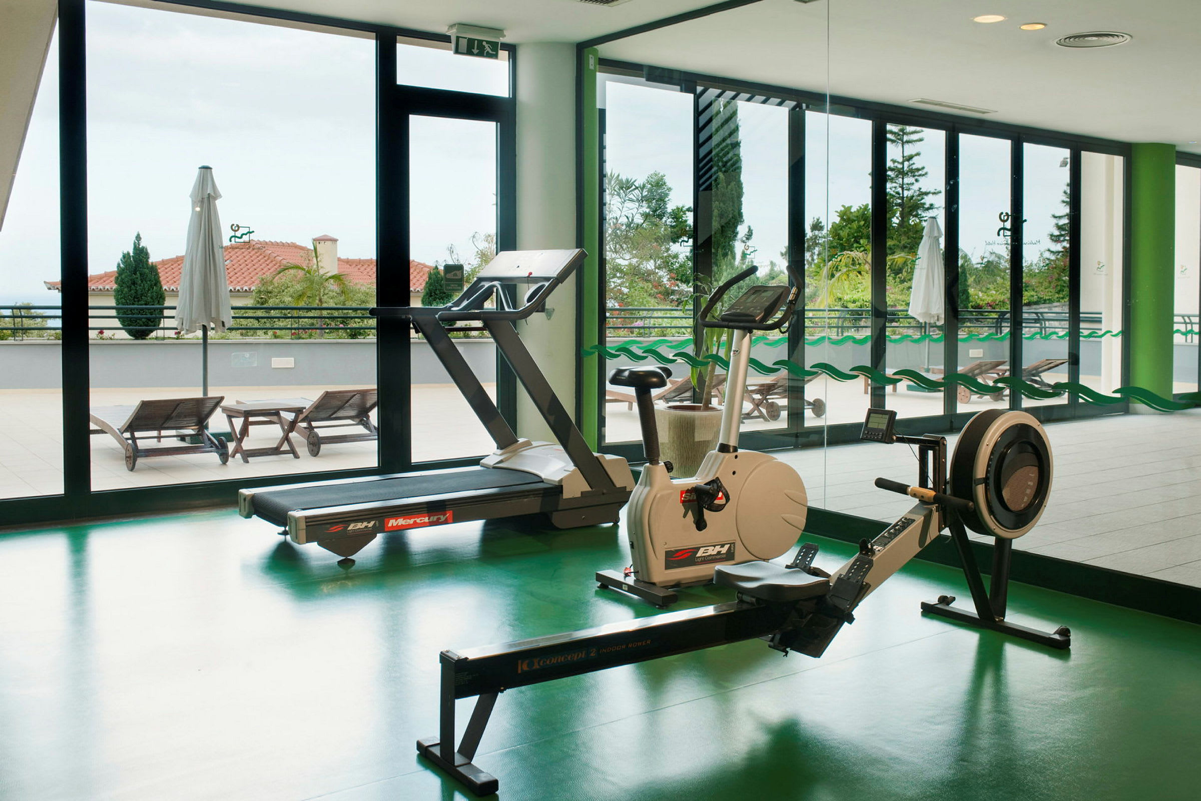 Inomhusgym med träningsutrustning framför stora fönster. (AI-genererad text)