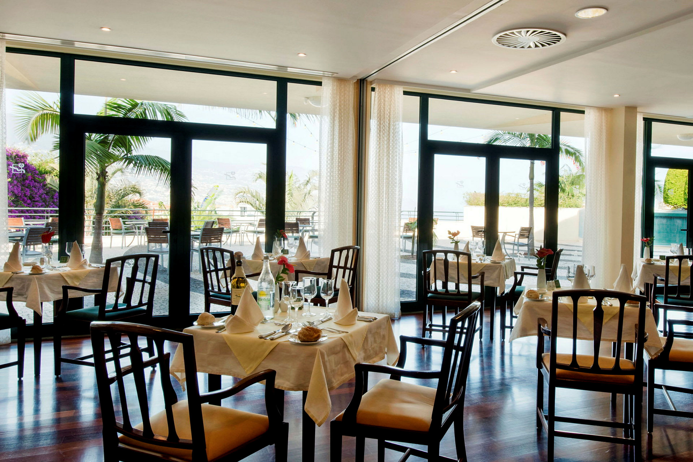 En trevlig restaurang med dukade bord och utsikt mot en veranda med palmträd. (AI-genererad text)