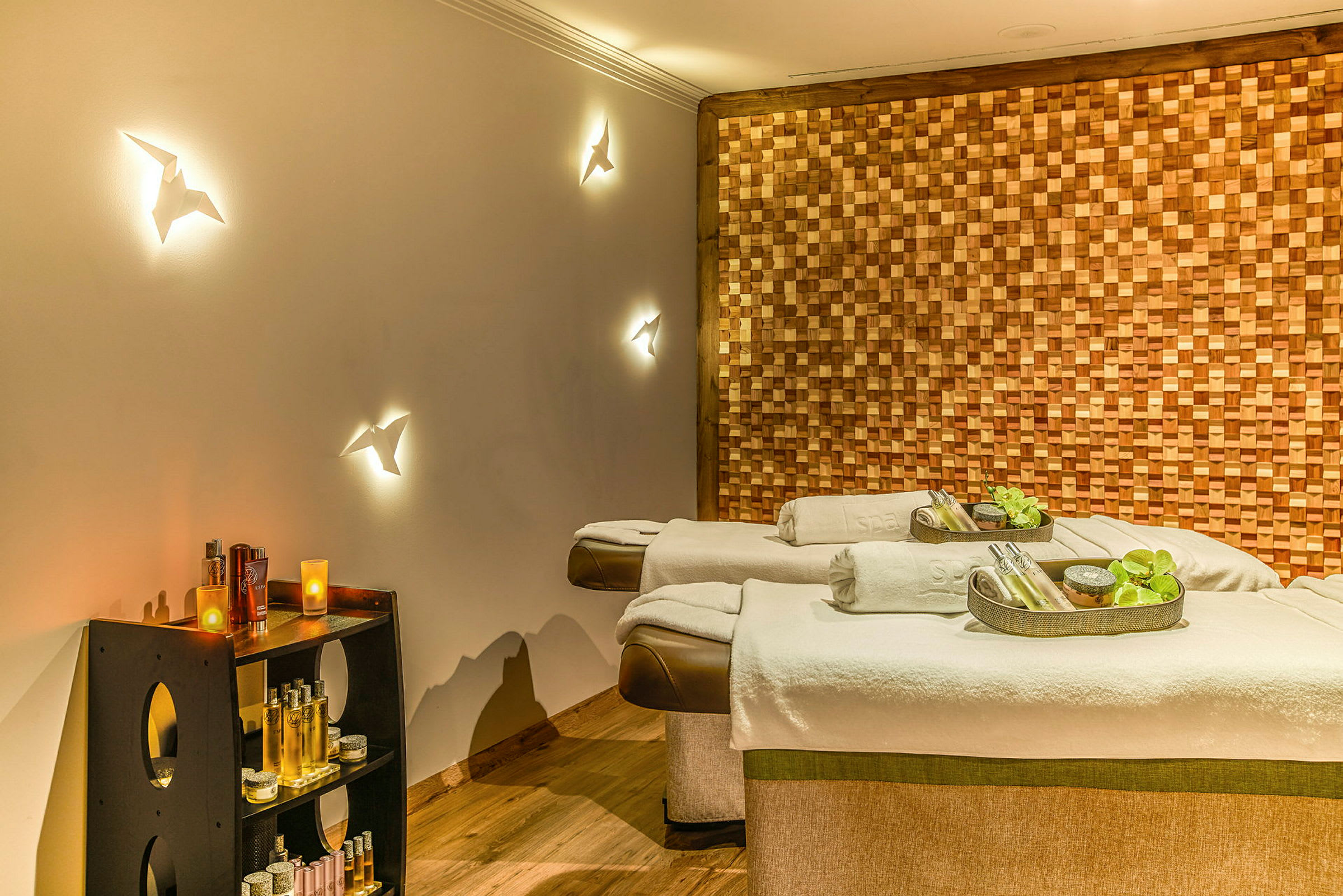 Två spa-massagebänkar med prydnadstillbehör, omgivet av ett träbeklätt väggpanel och hyllor med olika spa-produkter. (AI-genererad text)