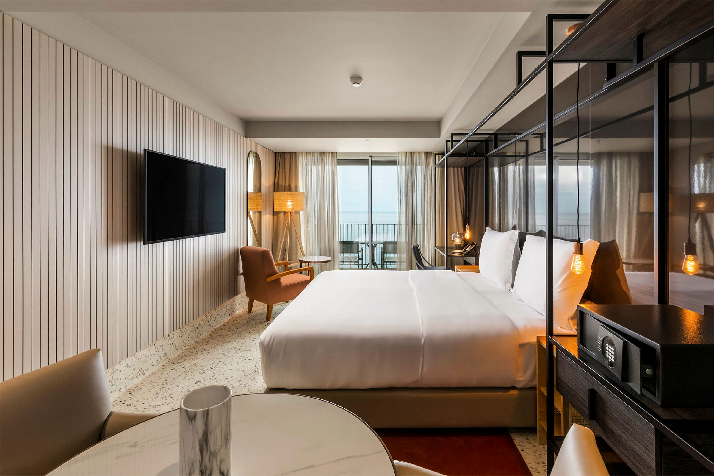 Hotellrum med dubbelsäng, sittmöbler och TV, samt balkong med utsikt. (AI-genererad text)