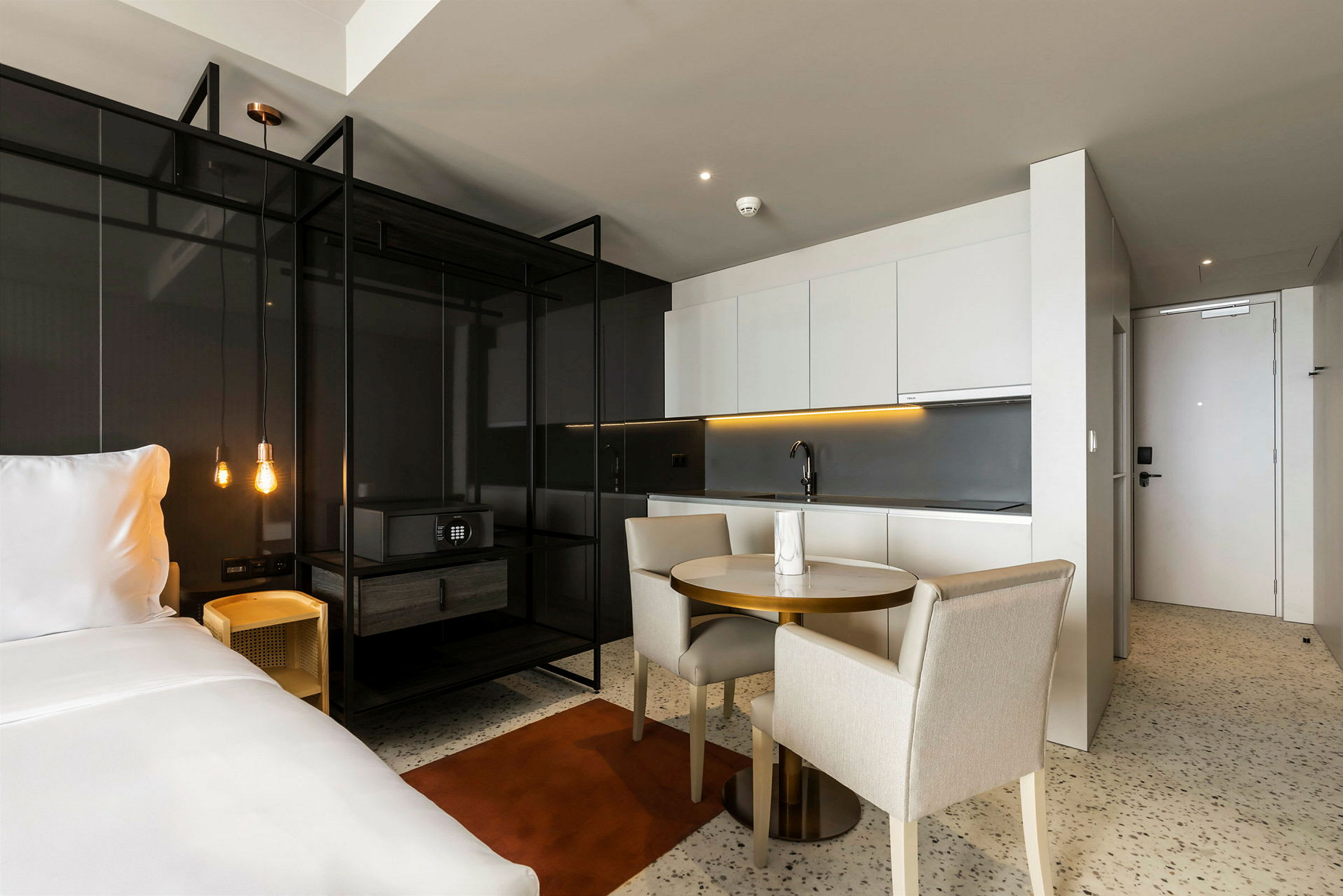 Ett modernt hotellrum med en öppen planlösning som inkluderar en dubbelsäng, kök och matbord. (AI-genererad text)