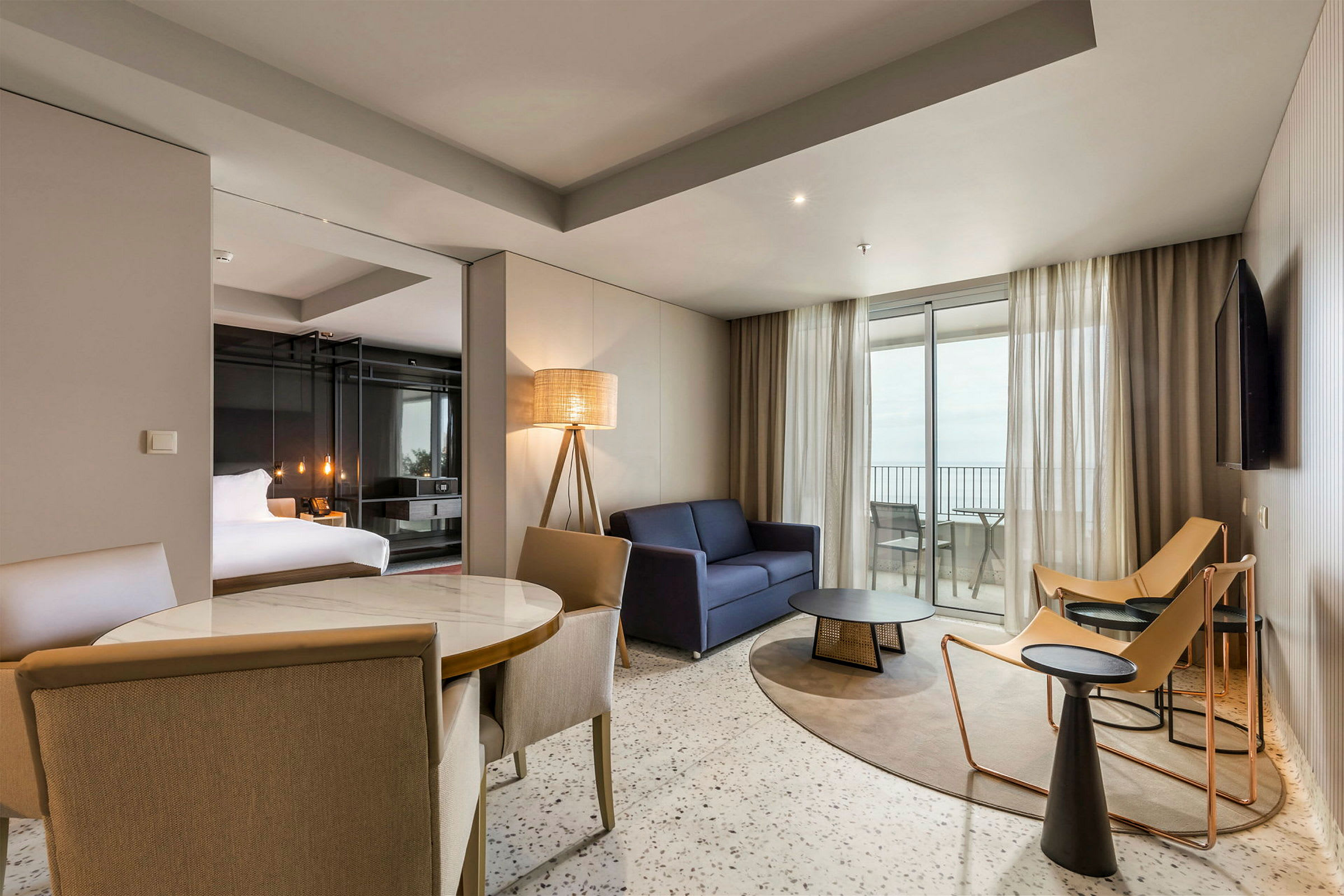 Ett modernt hotellrum med sittgrupp, säng och utsikt mot balkongen. (AI-genererad text)