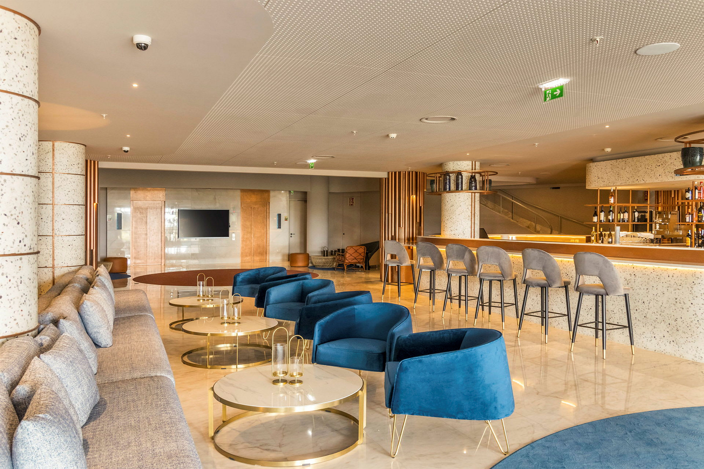 Modernt hotellrum med blå fåtöljer, soffor och ett bardområde. (AI-genererad text)