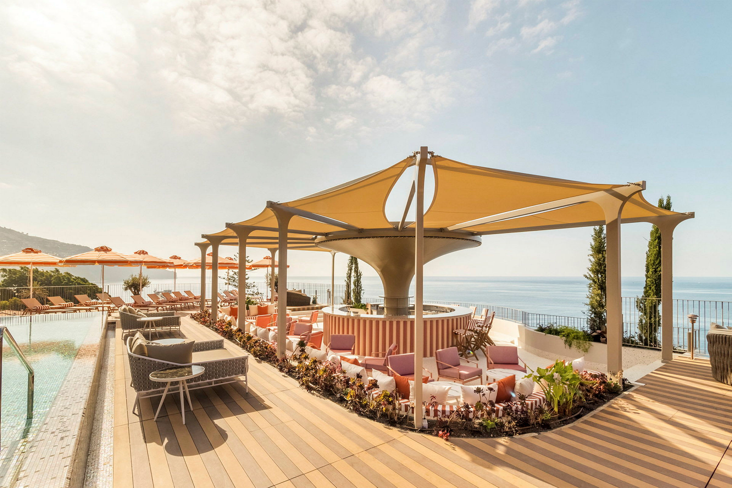 En terrass med pool, solstolar, parasoller och sittplatser under ett skuggande tak. Utsikt mot havet. (AI-genererad text)
