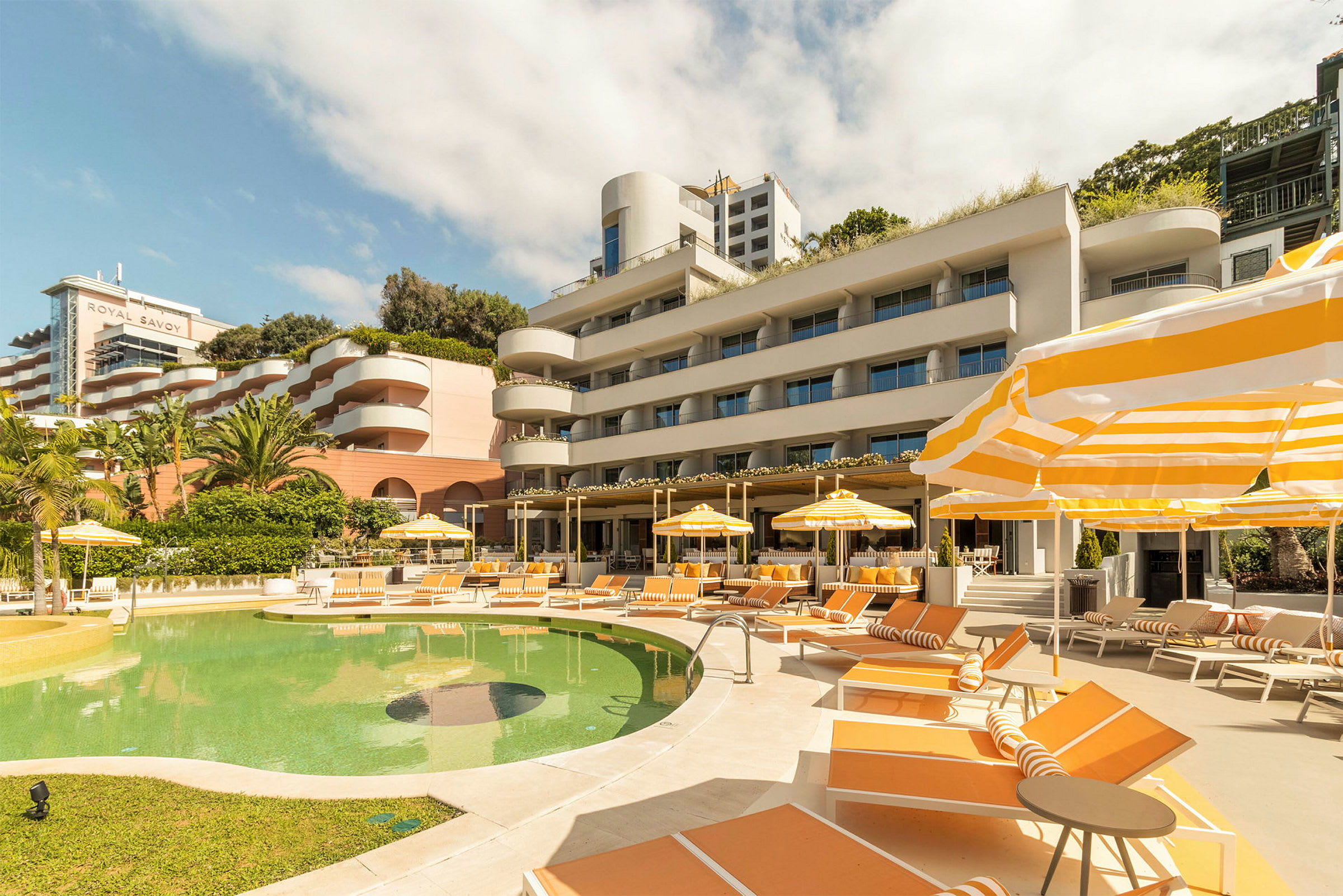 Utomhuspool med solstolar och parasoller framför hotellbyggnad. (AI-genererad text)