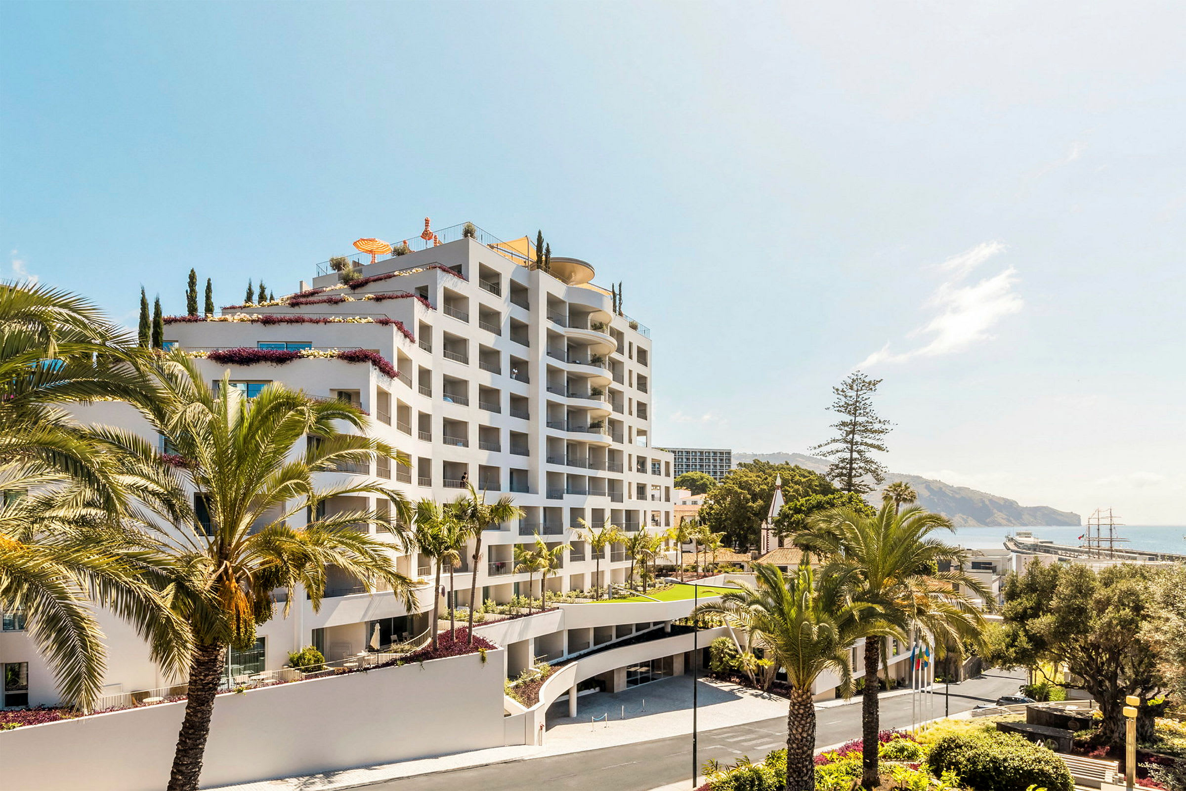 Ett fler våningshotell omgiven av palmer, med havet i bakgrunden. (AI-genererad text)