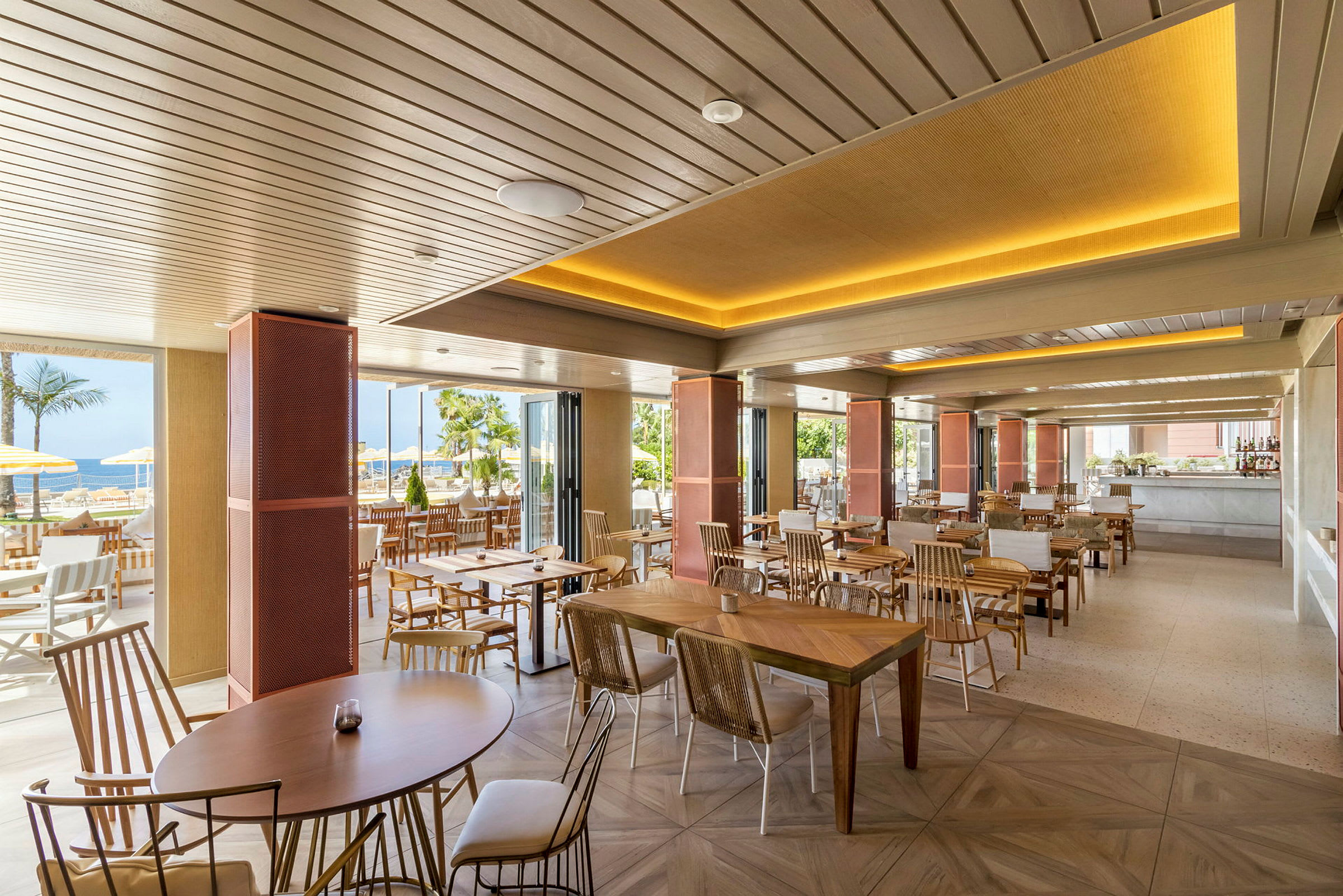 En modern restaurang med träbord och stolar, öppet mot en utomhusmiljö med palmer. (AI-genererad text)
