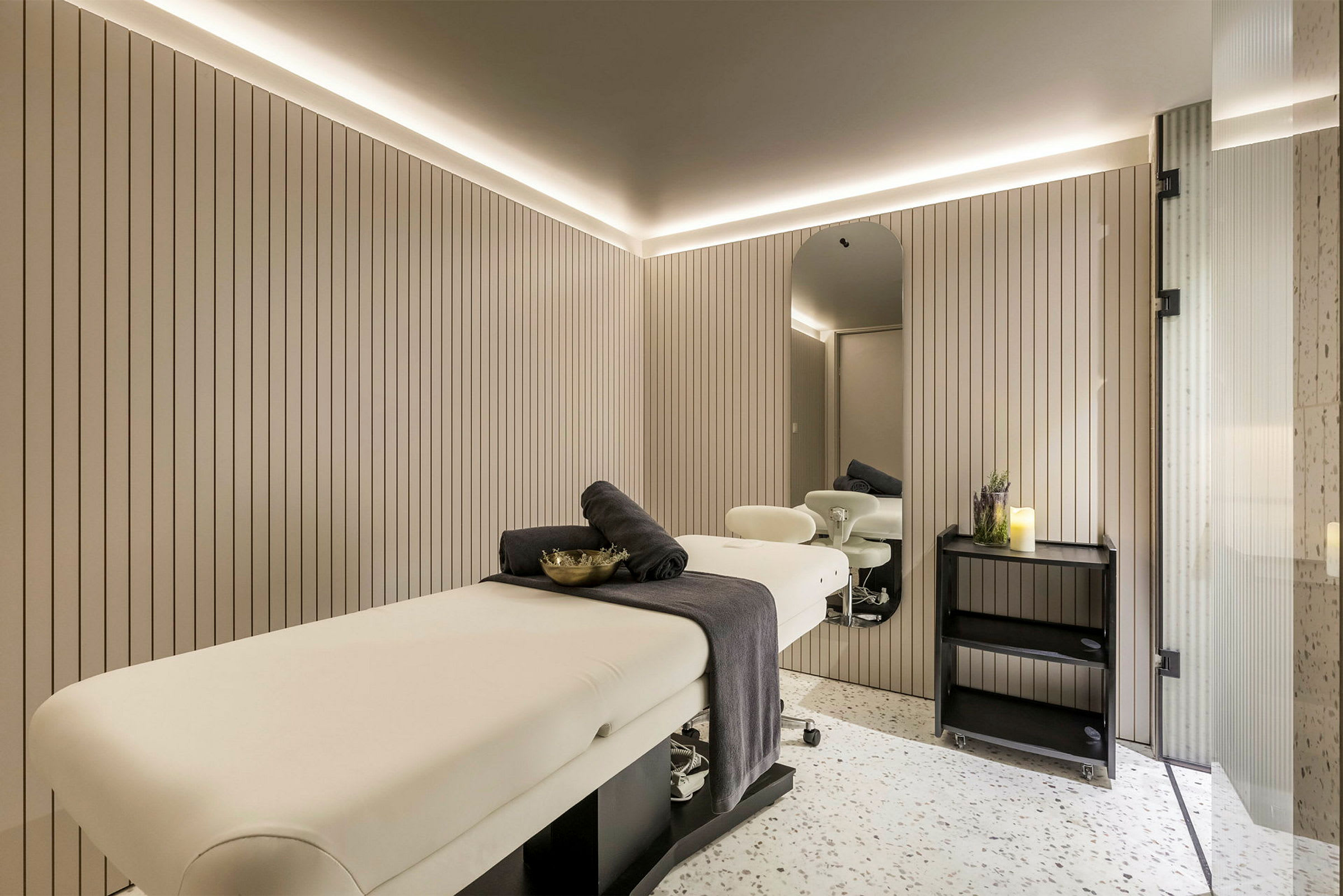 Ett modernt massagesrum med en bänk, dekorationer och spegel. (AI-genererad text)