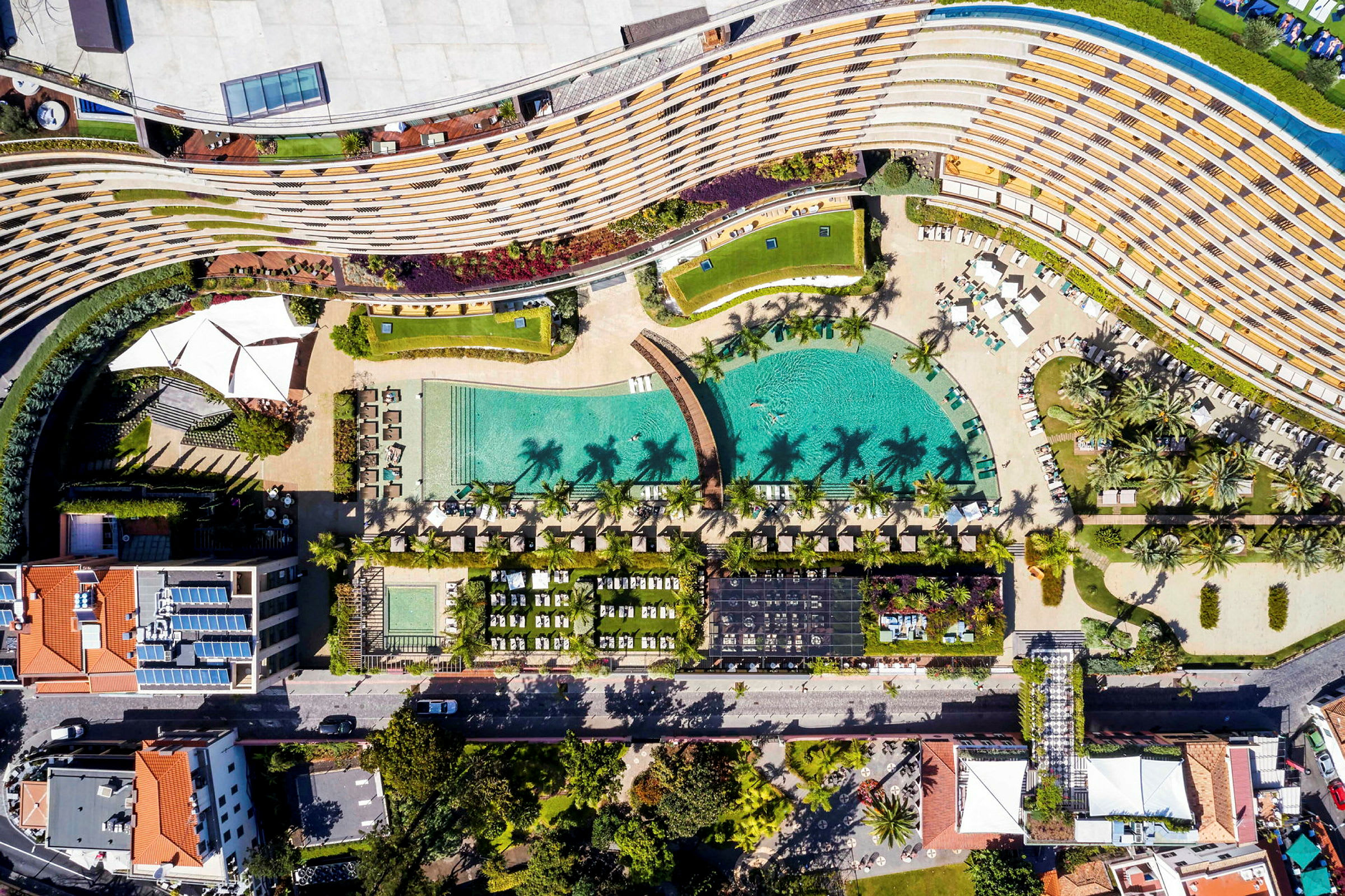 Flygfoto av ett hotellområde med pool, solstolar och trädgård. (AI-genererad text)