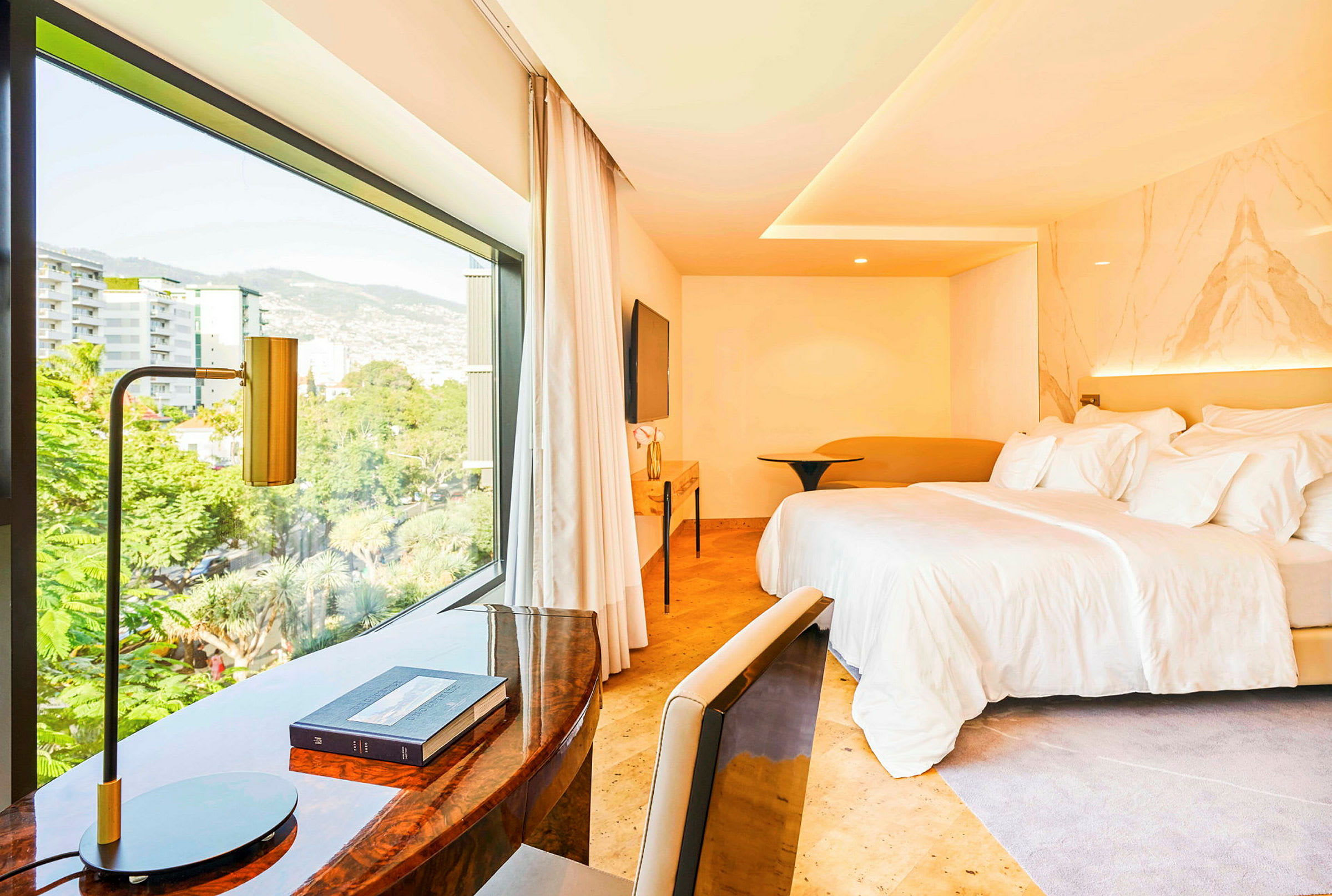 Ett hotellrum med en stor säng och ett skrivbord nära ett stort fönster som visar utsikten över staden. (AI-genererad text)