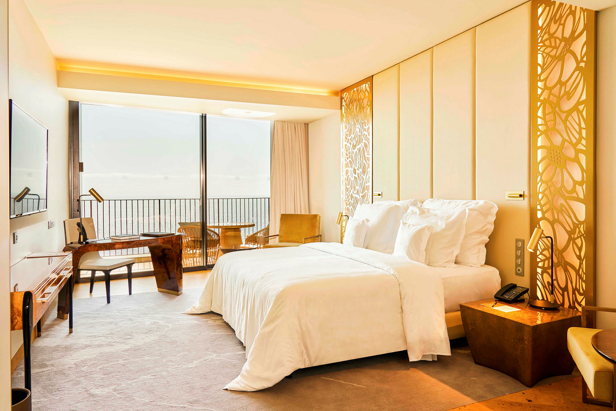 Hotellrum med en dubbelsäng, skrivbord och utsikt över havet genom en stor fönstervägg. (AI-genererad text)