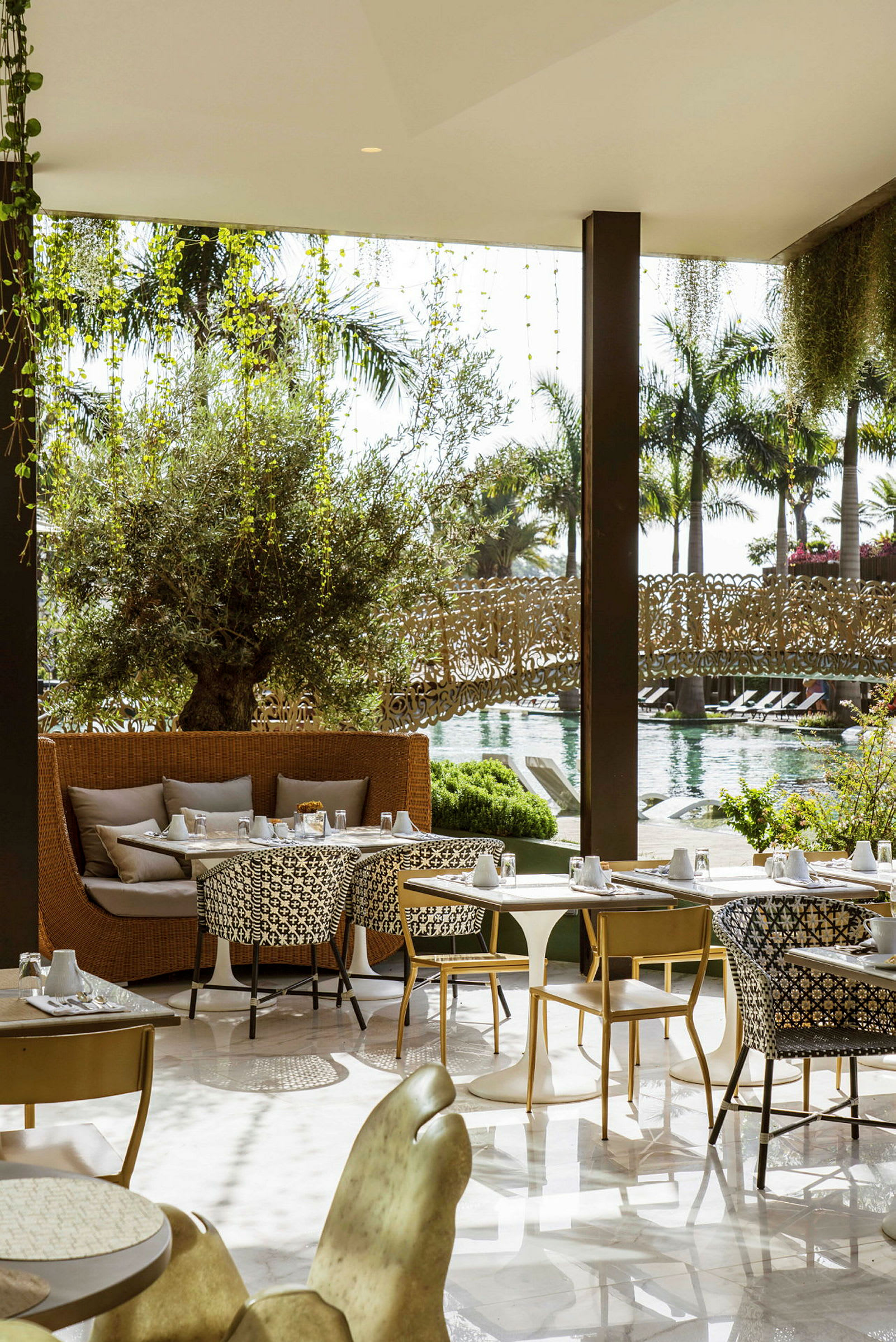 Restaurangområde med sittplatser och bord, utsikt mot en pool och grönska. (AI-genererad text)
