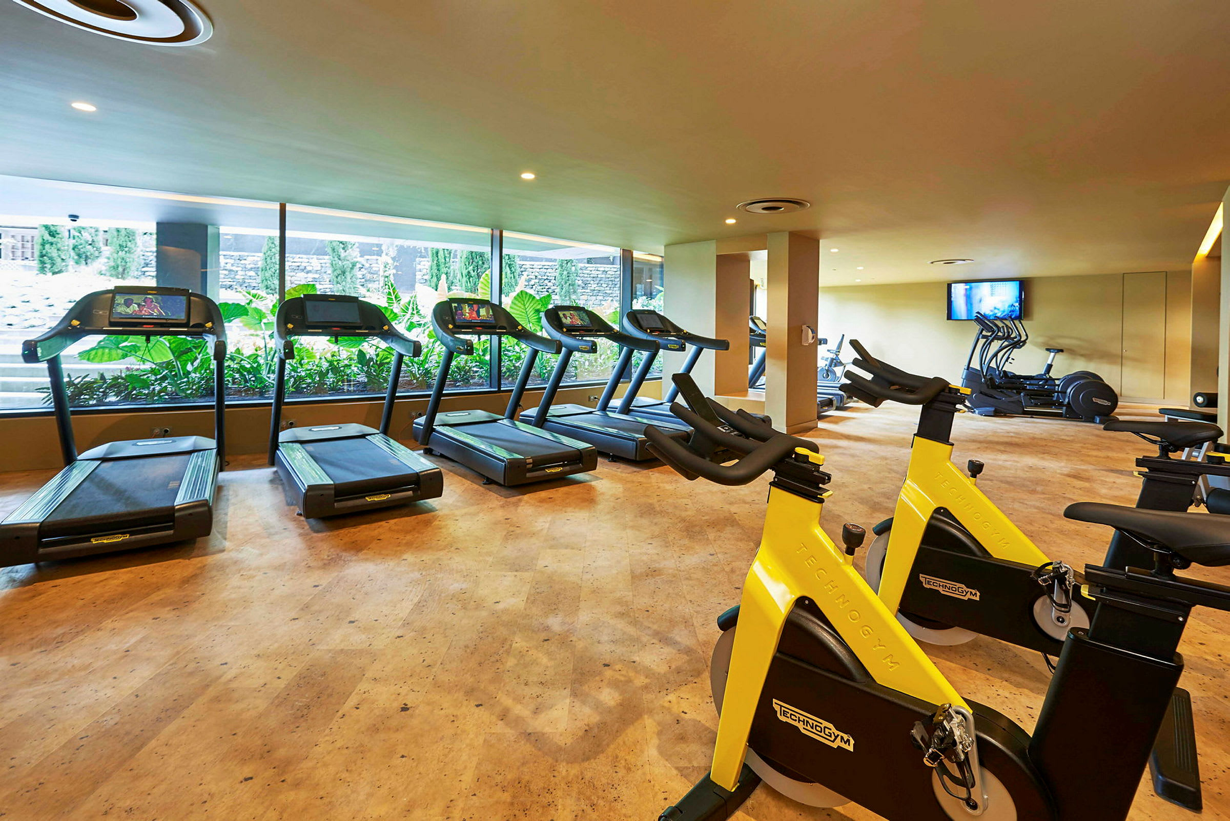 Gym med löpband och träningscyklar framför stora fönster. (AI-genererad text)
