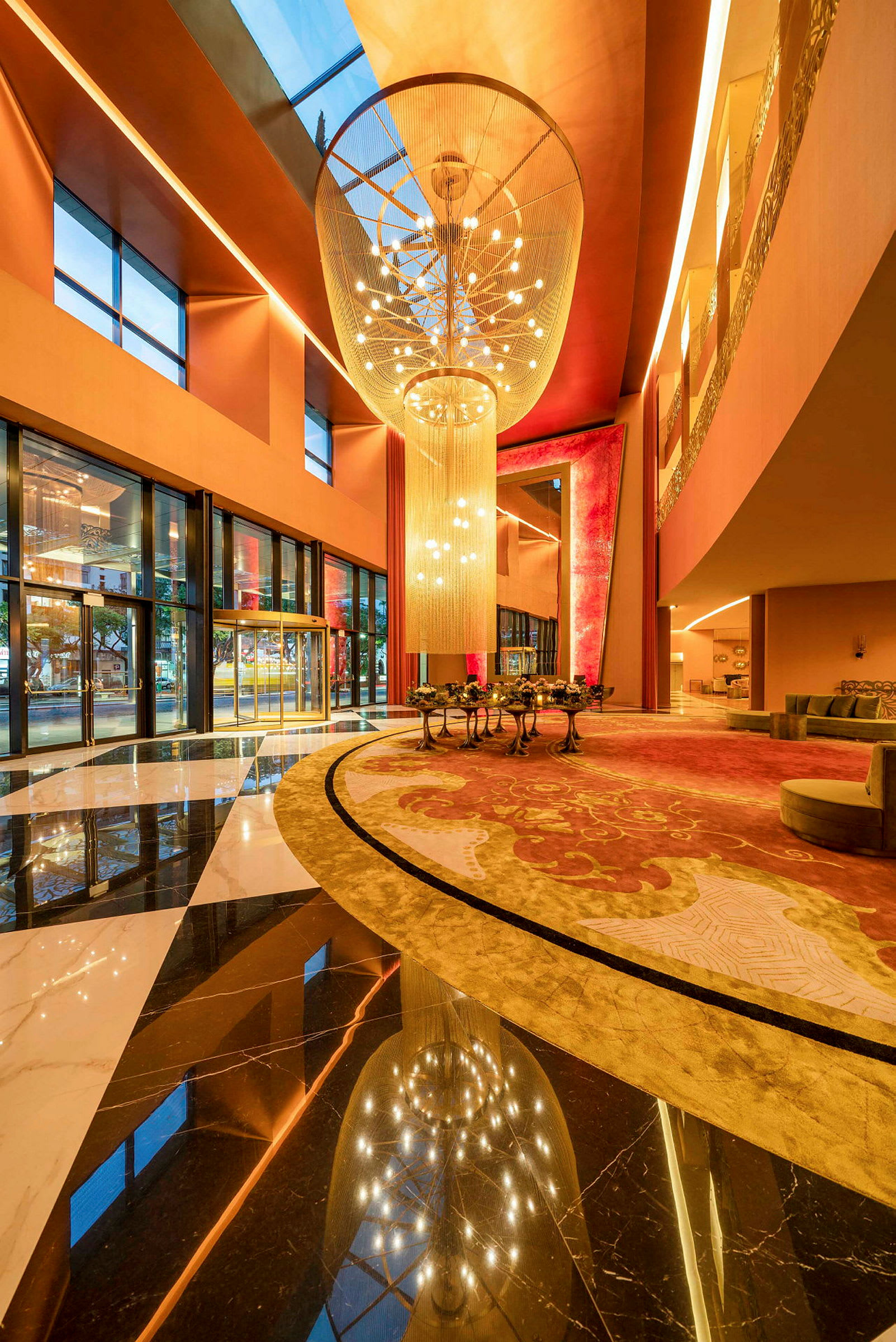 Ett hotellfoajé med stora fönster, färgglada mattor och en stor ljuskrona. (AI-genererad text)