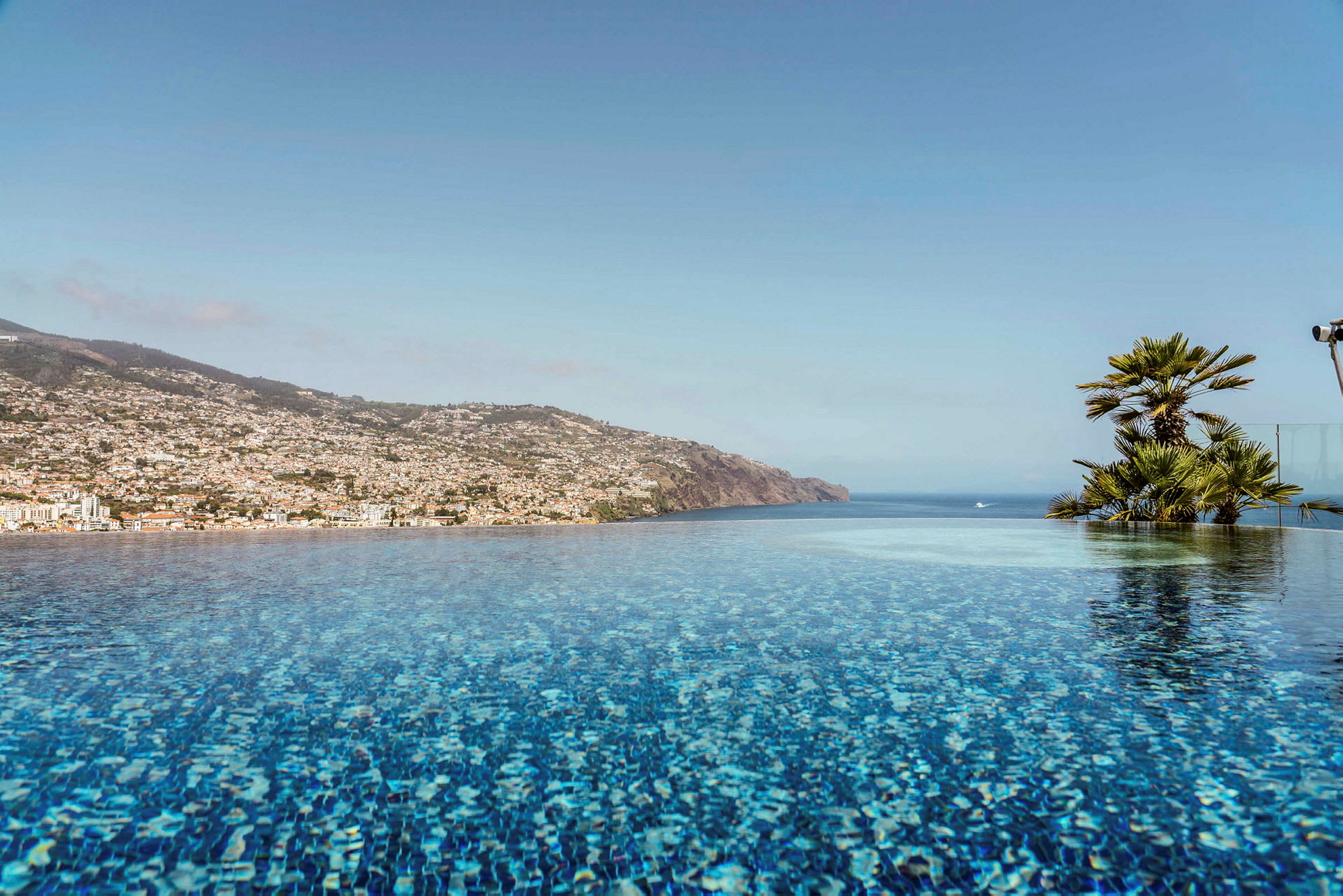 En infinitypool med utsikt mot havet och en bergsluttning fylld med byggnader. (AI-genererad text)