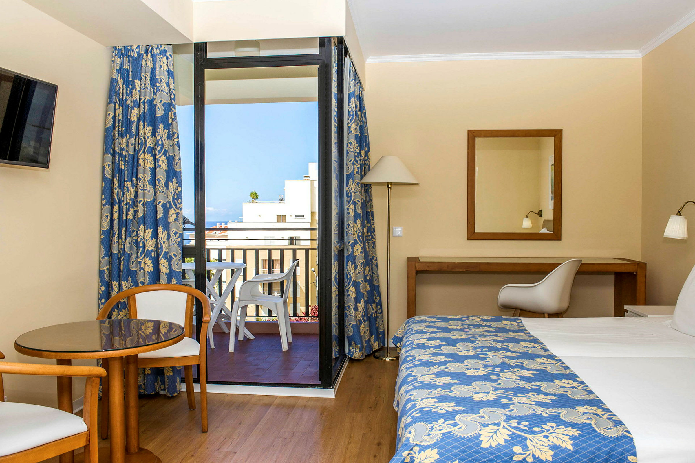 Hotellrum med en säng, ett bord och två stolar samt en balkong med utsikt. (AI-genererad text)
