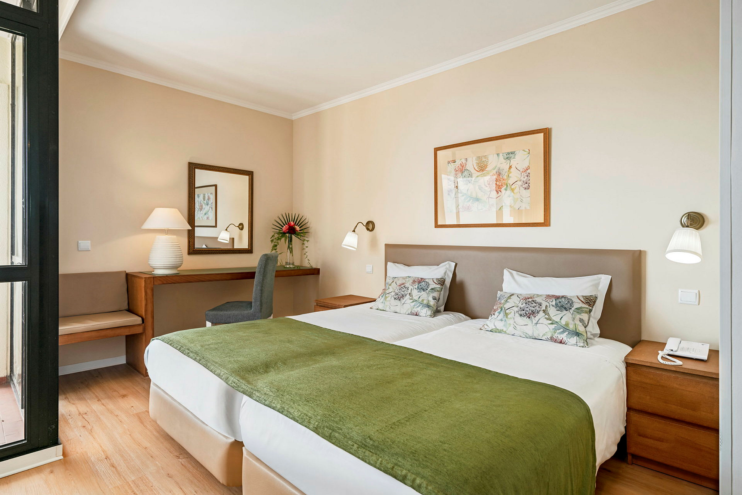 Bild av ett hotellrum med två enkelsängar klädda i vita sängkläder och gröna överkast, ett skrivbord med spegel och en stol i bakgrunden. (AI-genererad text)