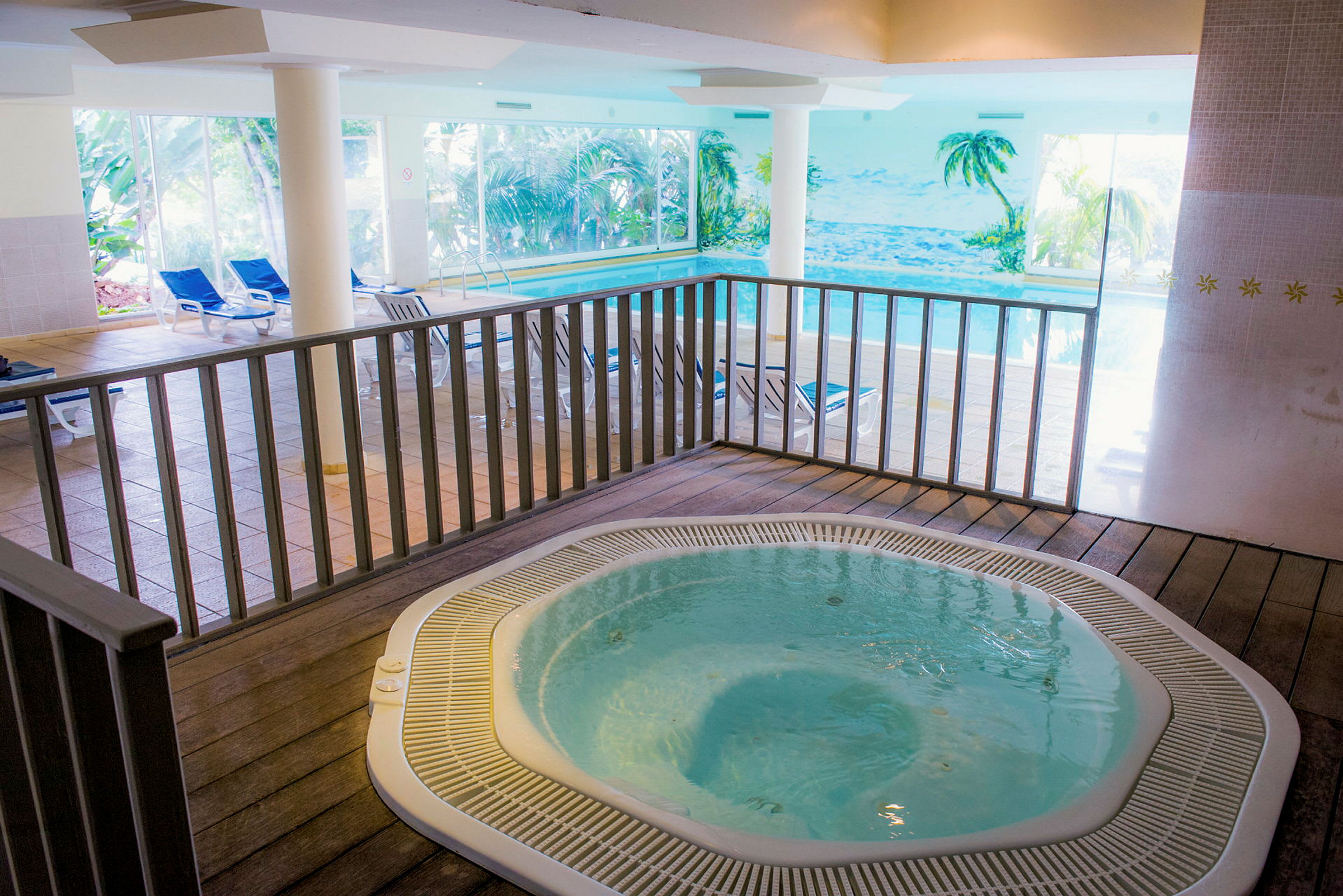 Interiör med en jacuzzi och en pool samt solstolar i bakgrunden. (AI-genererad text)