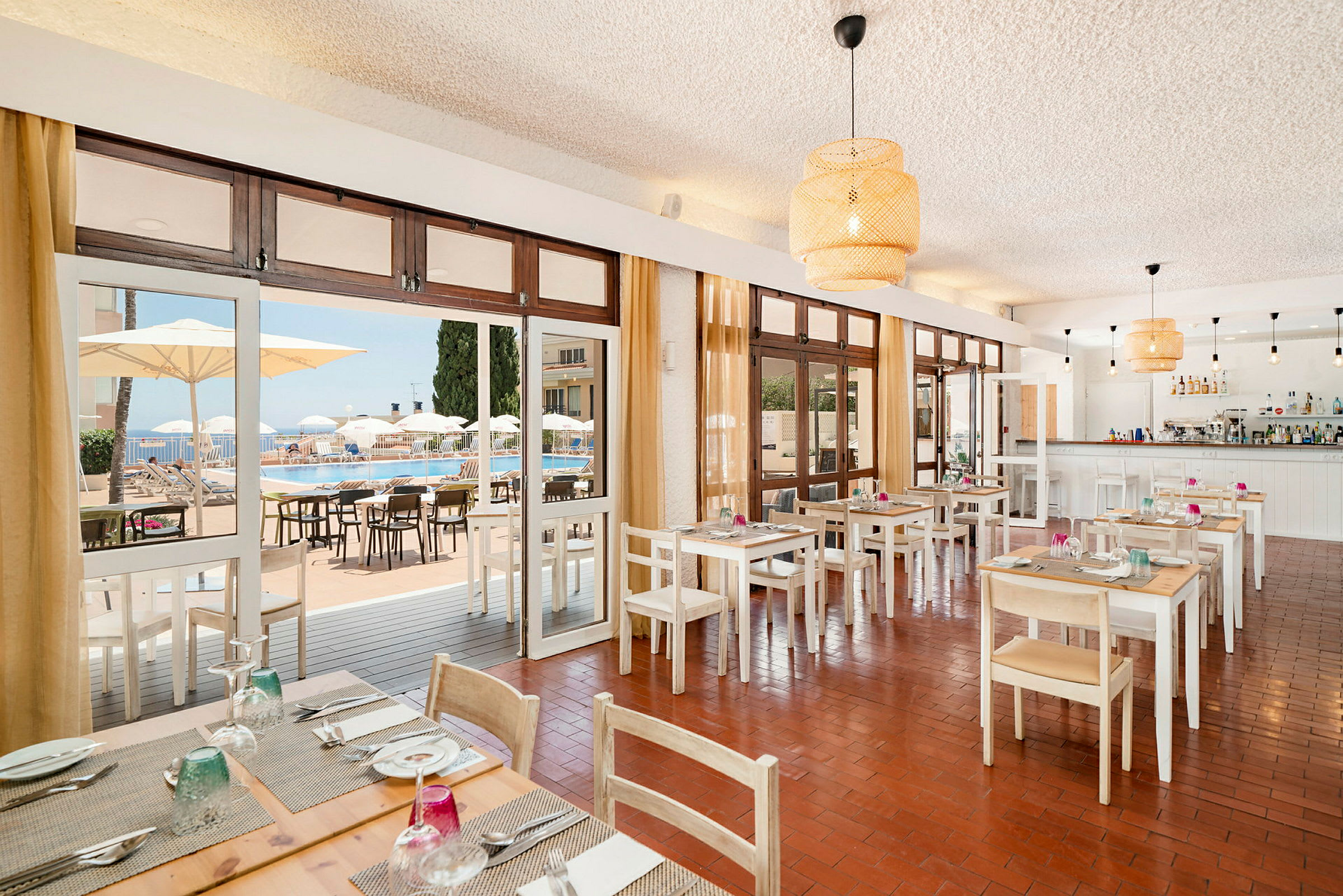 En restaurang med dukade bord och utsikt mot en pool genom glasdörrar. (AI-genererad text)