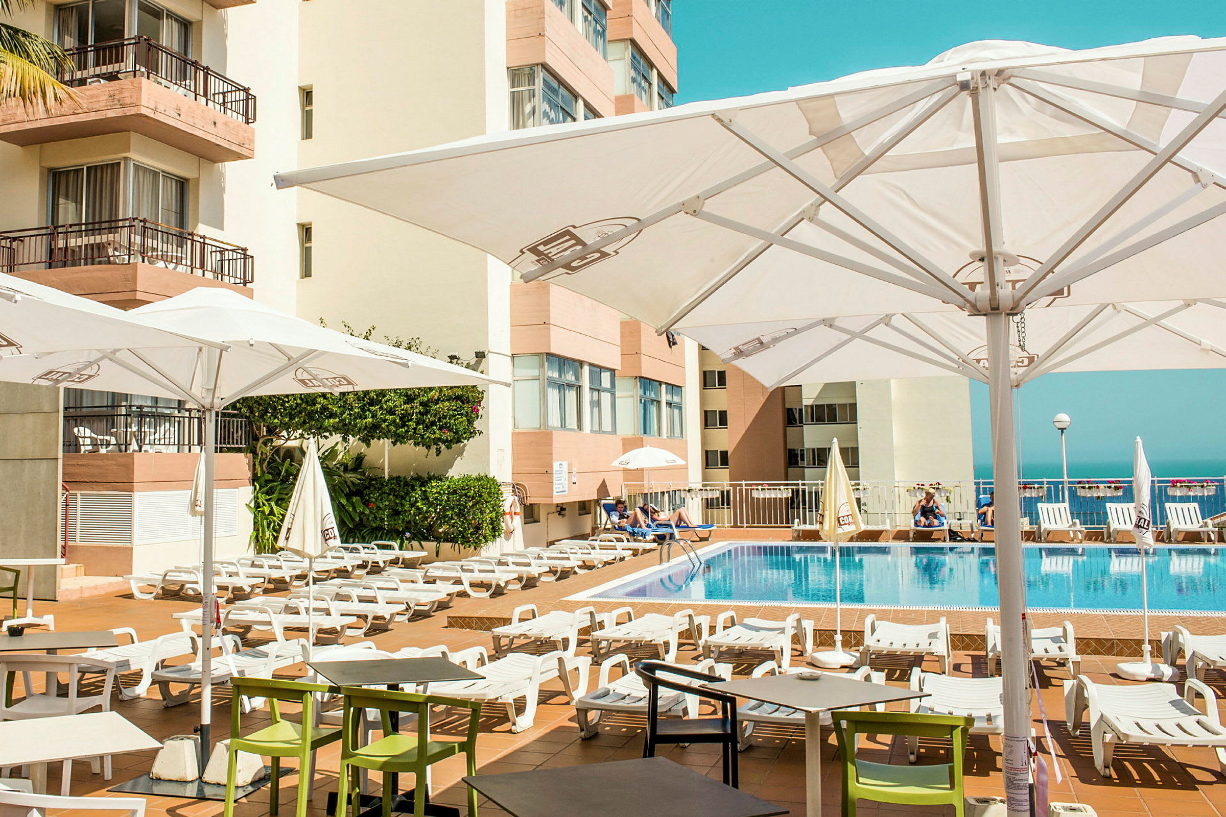 Utomhuspoolområde med solstolar och parasoller vid ett hotell. (AI-genererad text)