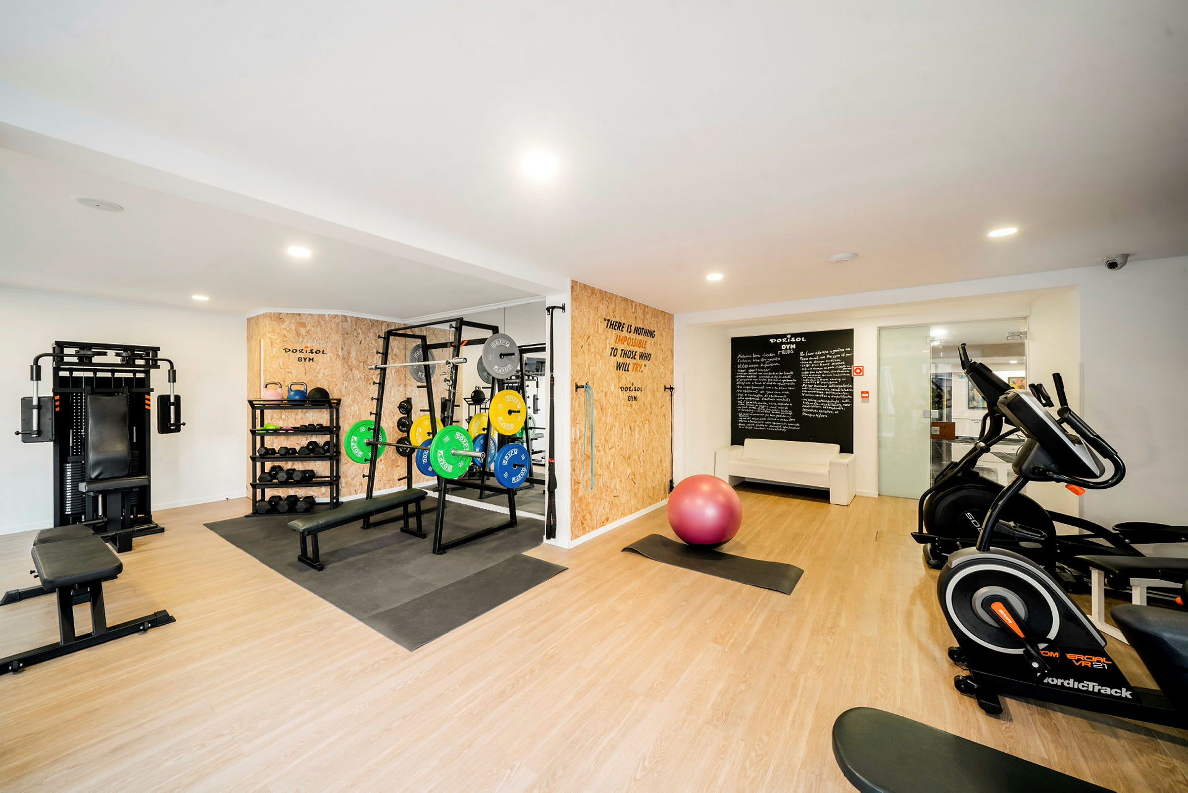 Ett gym med träningsmaskiner, vikter och en rosa balansboll. (AI-genererad text)