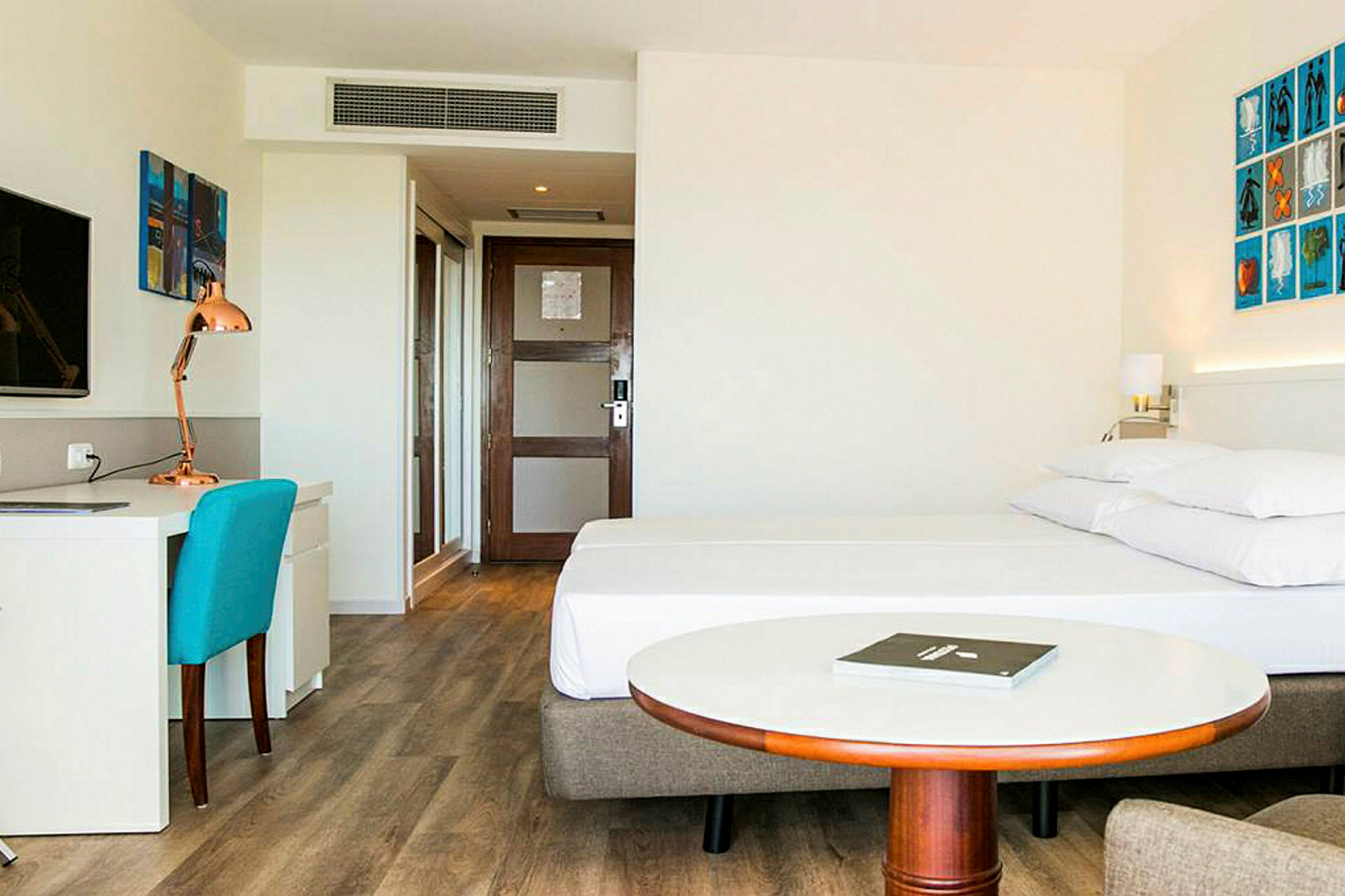 Hotellrum med en säng, skrivbord och stol, samt ett runt bord framför sängen. (AI-genererad text)