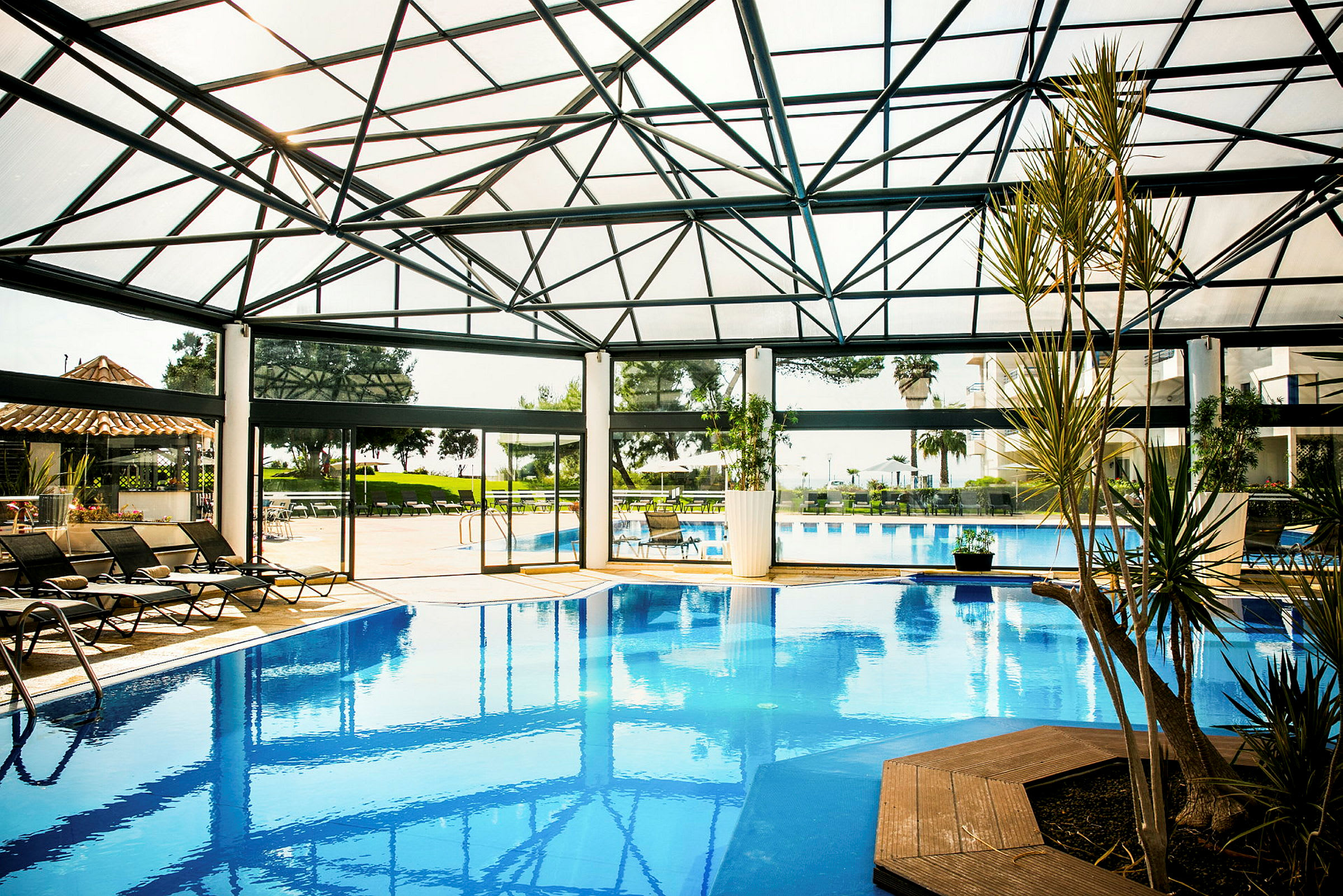 Poolområde med modern glaskonstruktion, solstolar och växter. (AI-genererad text)