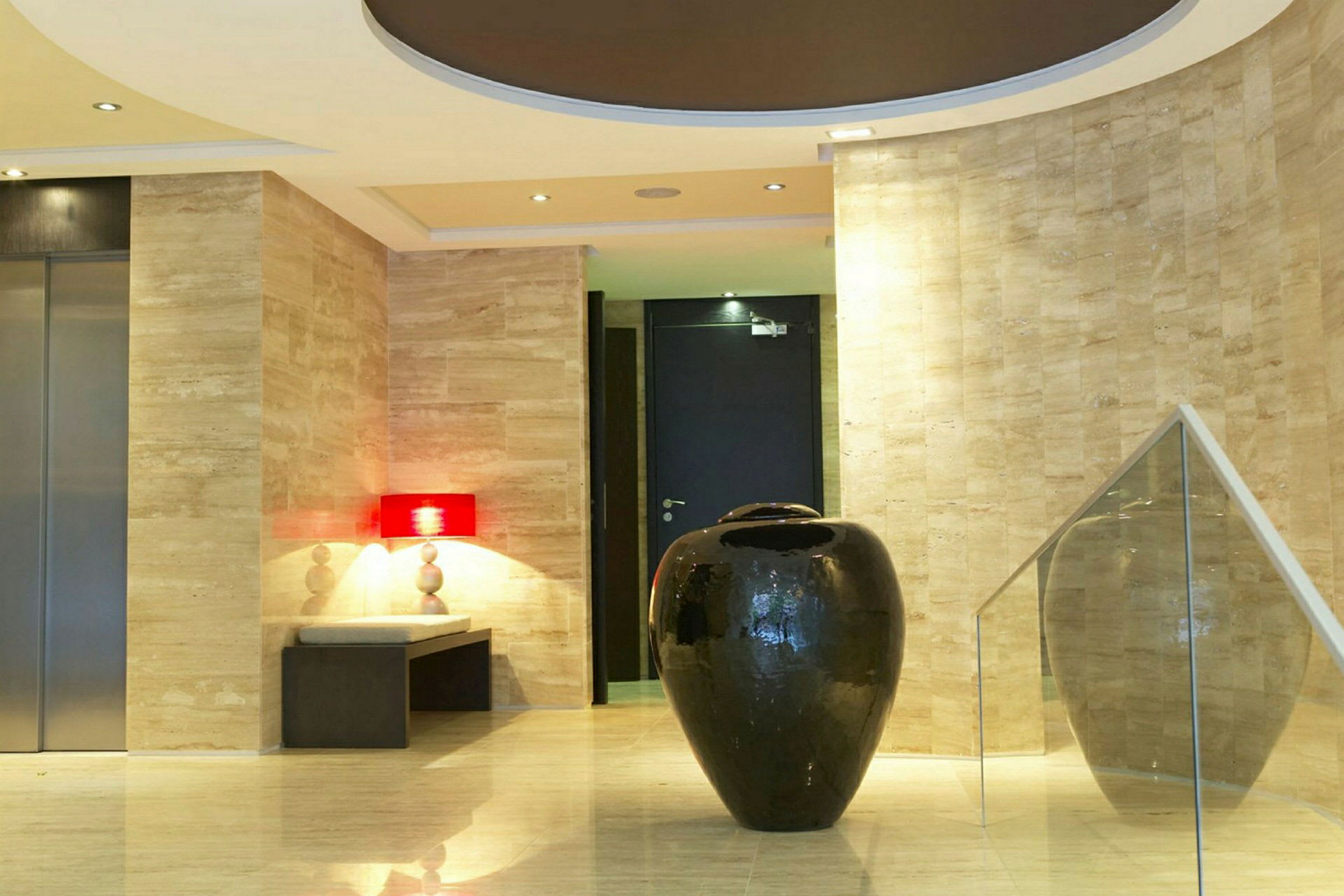En hotellobby med en stor svart dekorativ vas i förgrunden, omgiven av marmordetaljer och modern design. (AI-genererad text)