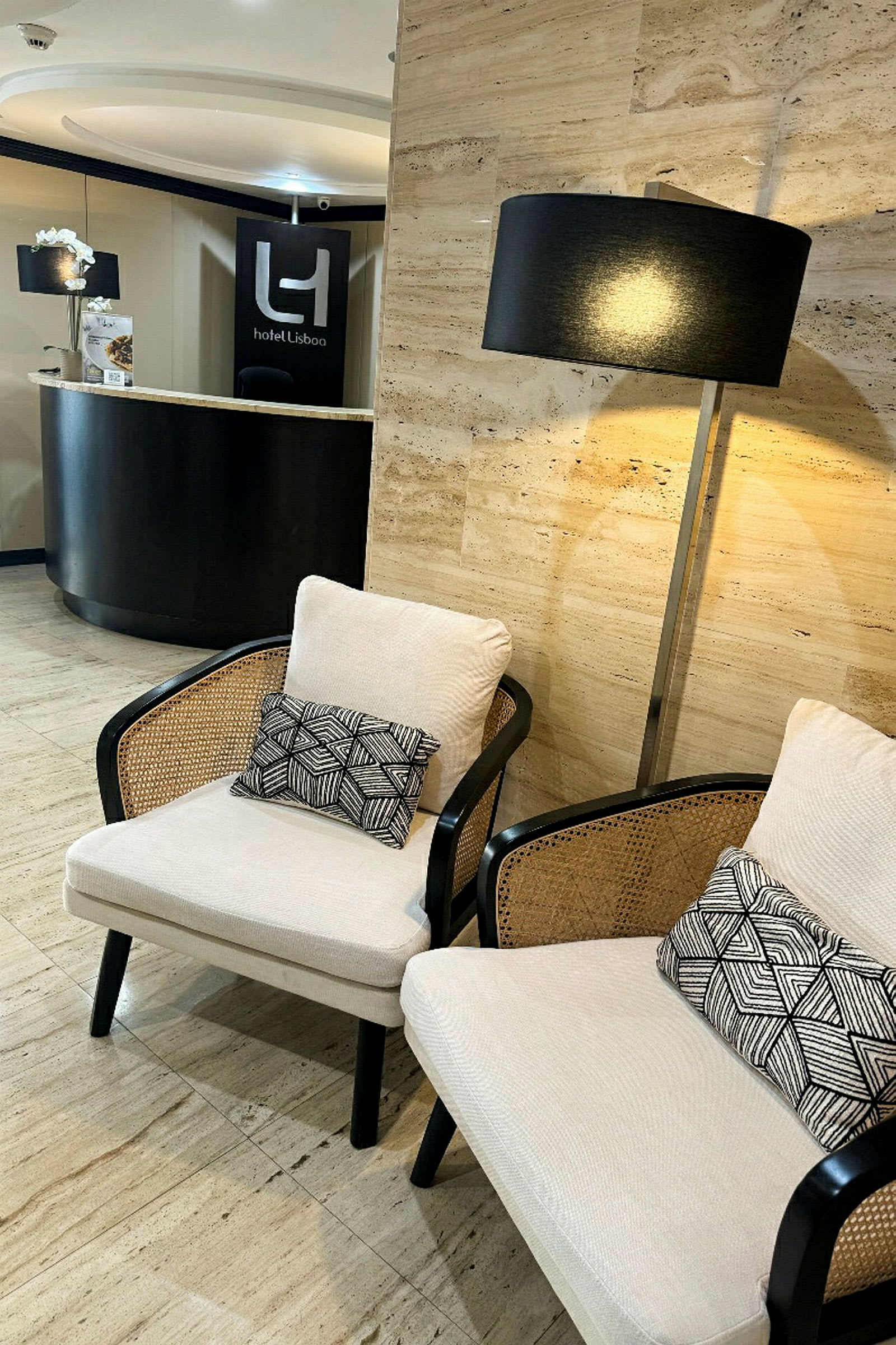 Två stolar med dekorativa kuddar, en golvlampa och en receptionsdisk med en skylt som visar "Hotel Lisboa". (AI-genererad text)
