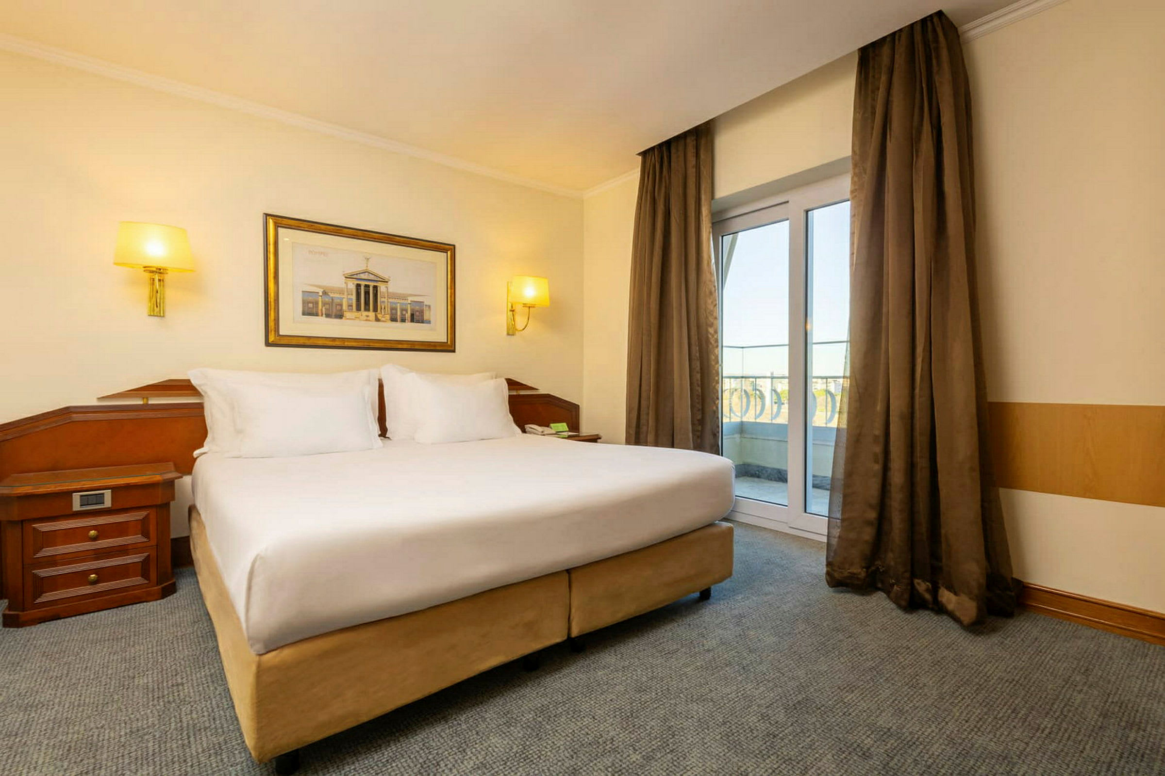 Ett hotellrum med en stor dubbelsäng och fönster som vetter mot balkongen. (AI-genererad text)