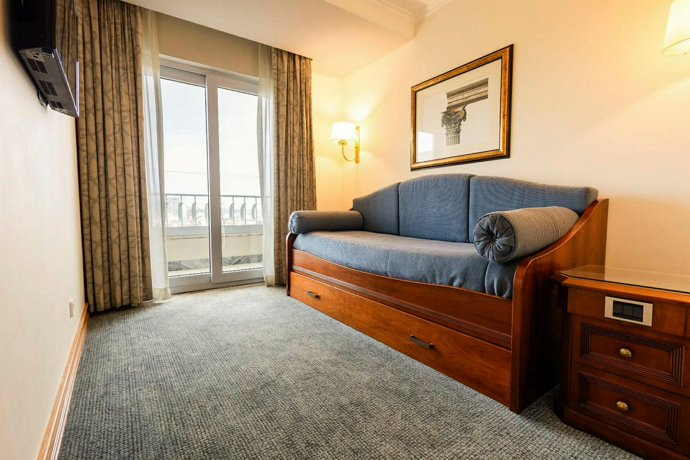 Ett rum med en bäddsoffa, ett sängbord och en balkongdörr. (AI-genererad text)