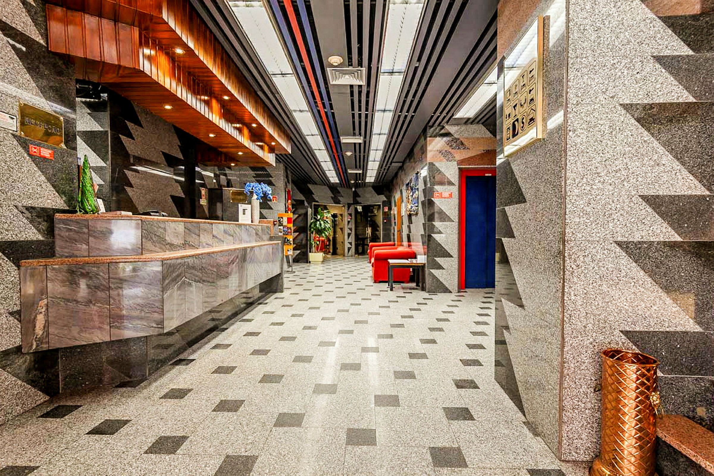 Hotellobby med marmorinredning, ett receptionsområde och röda sittmöbler. (AI-genererad text)