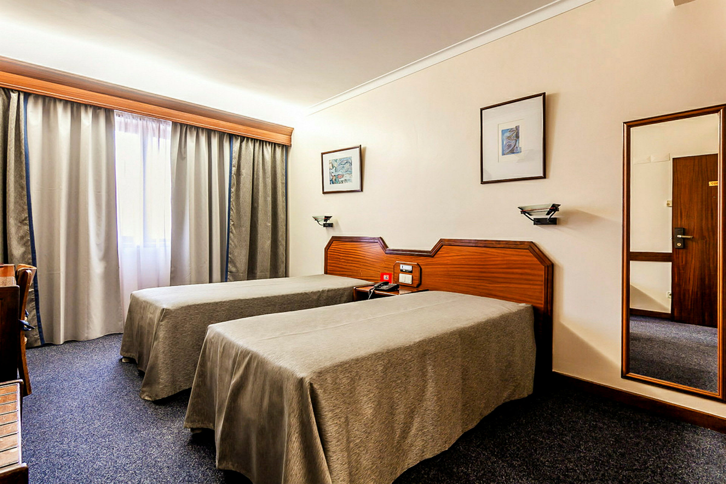Bild av ett hotellrum med två enkelsängar, ett skrivbord och ett fönster med gardiner. (AI-genererad text)
