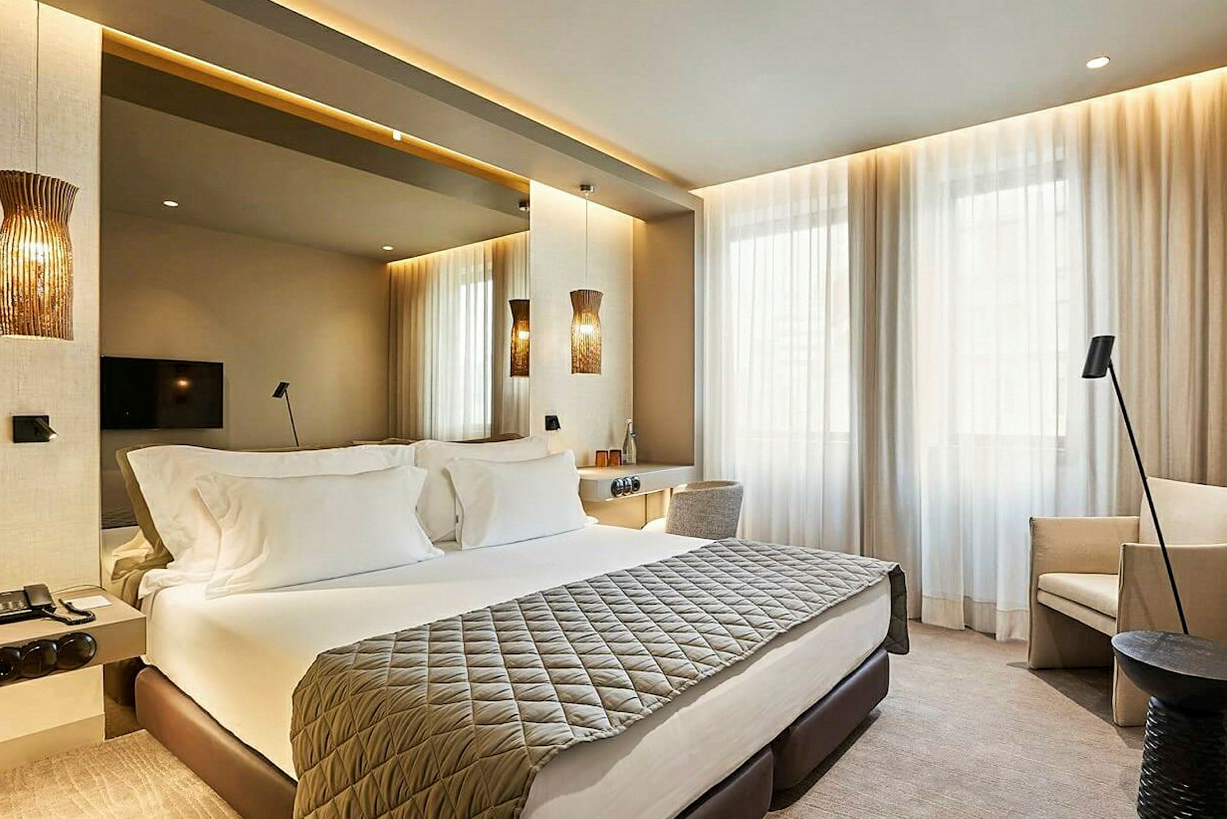 Ett modern inrett hotellrum med en dubbelsäng, väggmonterad TV och stora fönster med ljusa gardiner. (AI-genererad text)