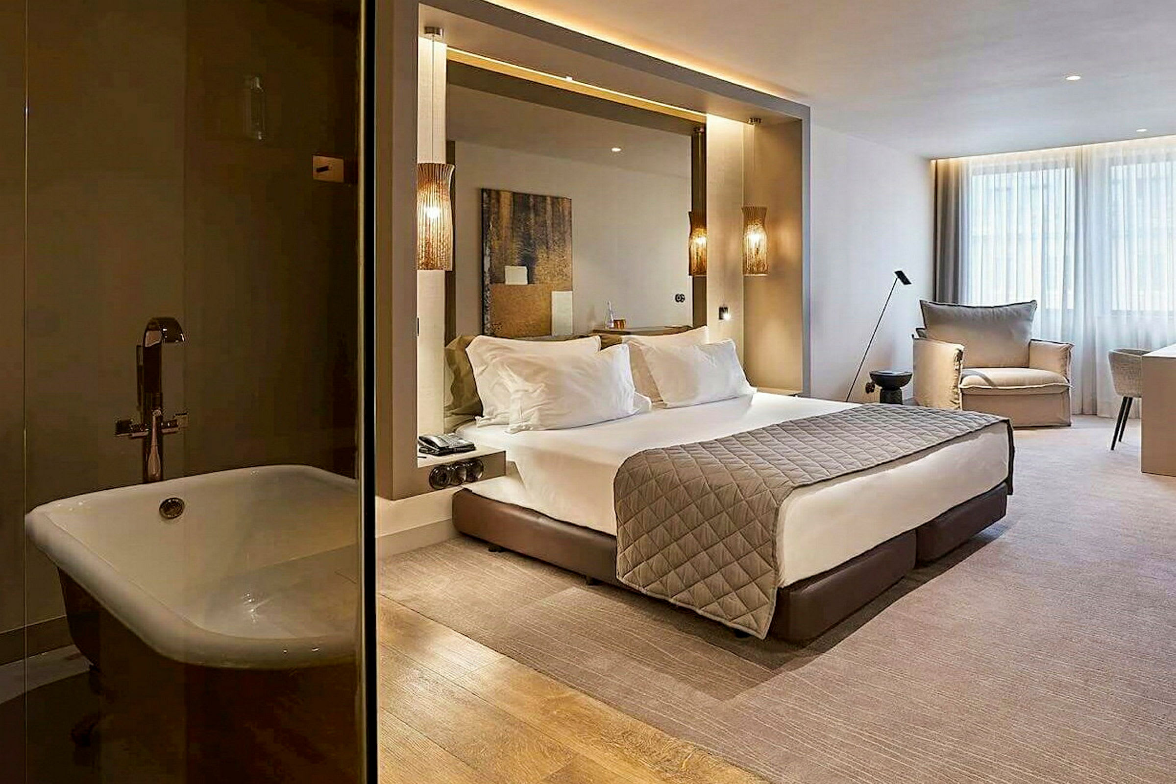 Ett modernt hotellrum med en stor säng, sittmöbler och fönster. Till vänster syns ett badkar. (AI-genererad text)
