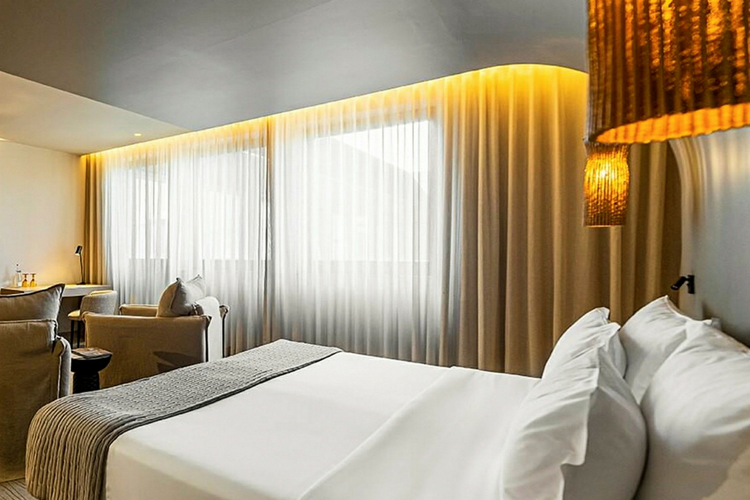 Ett hotellrum med en säng, sittgrupp och stora fönster med gardiner. (AI-genererad text)