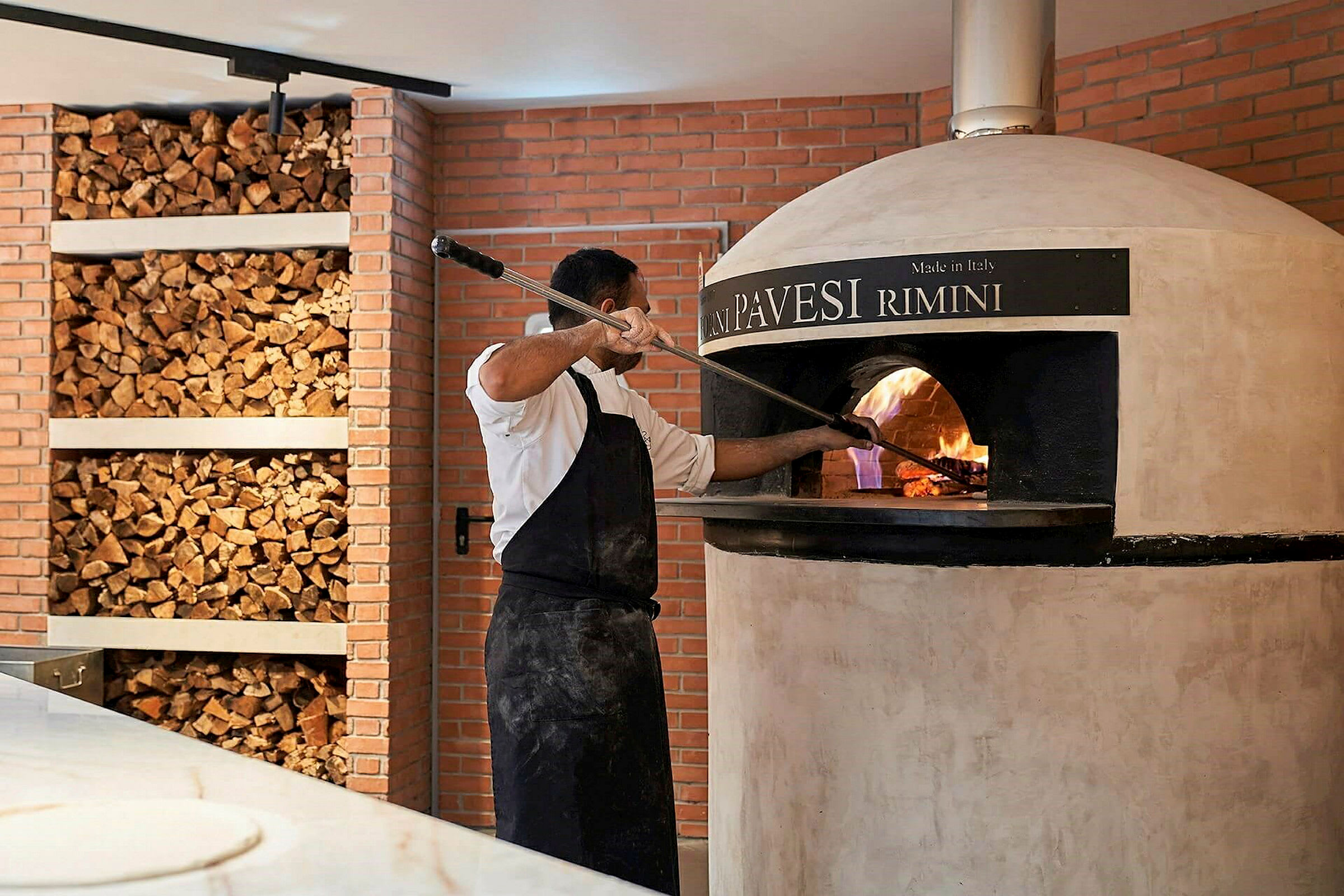 Person bakar pizza i vedeldad ugn. (AI-genererad text)