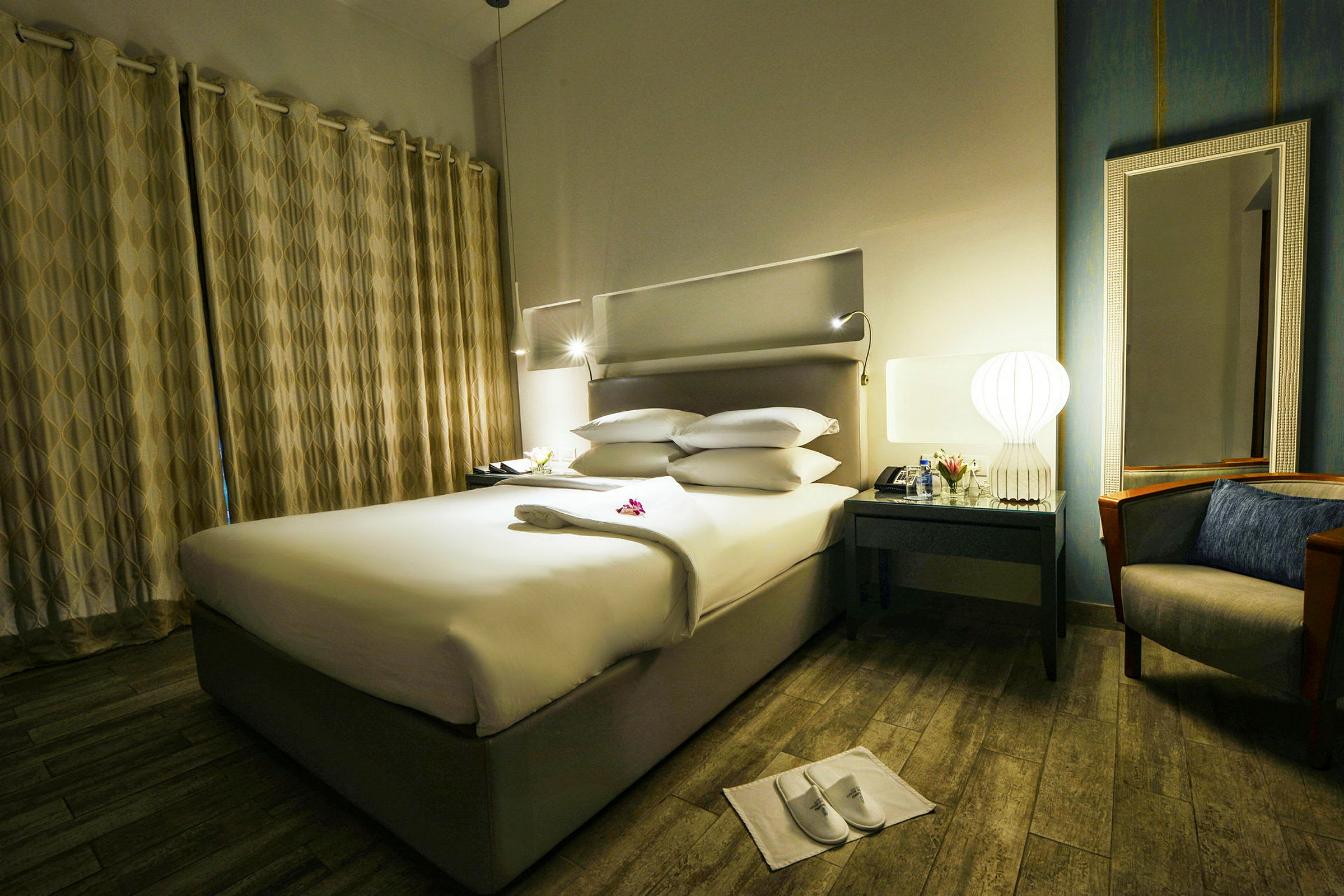Ett hotellrum med en bäddad säng, bord med lampa och spegel samt en fåtölj intill. (AI-genererad text)