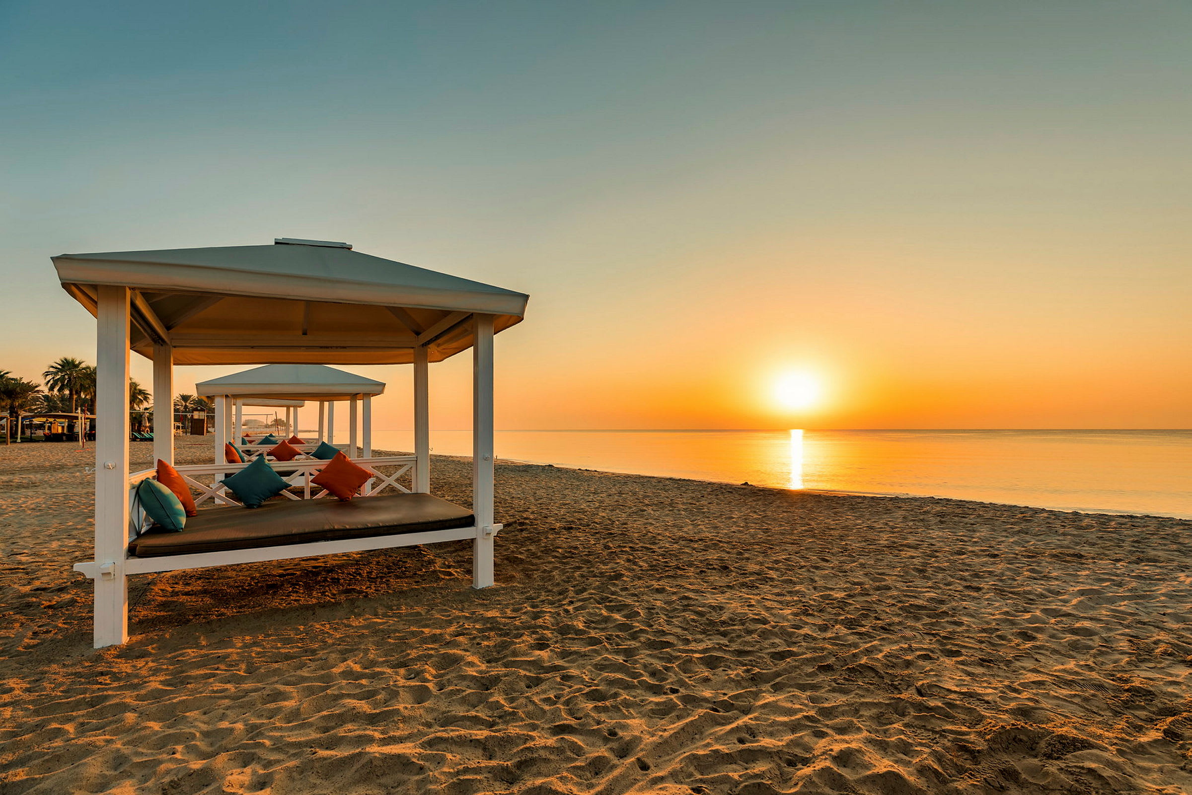 Strand med vita paviljonger och färgglada kuddar i solnedgången. (AI-genererad text)