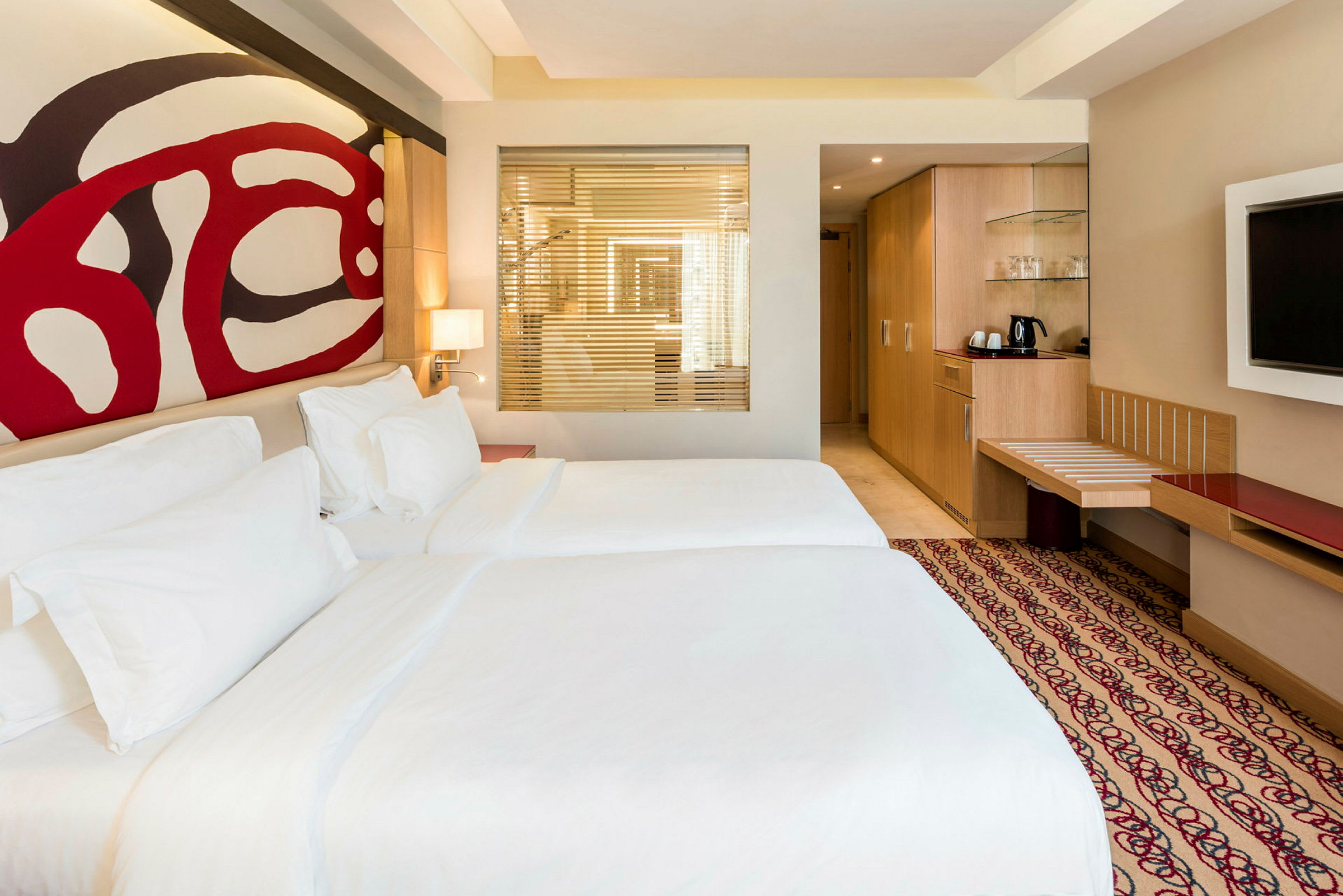 Hotellrum med två sängar, abstrakt väggdekoration, och en tv på väggen. (AI-genererad text)