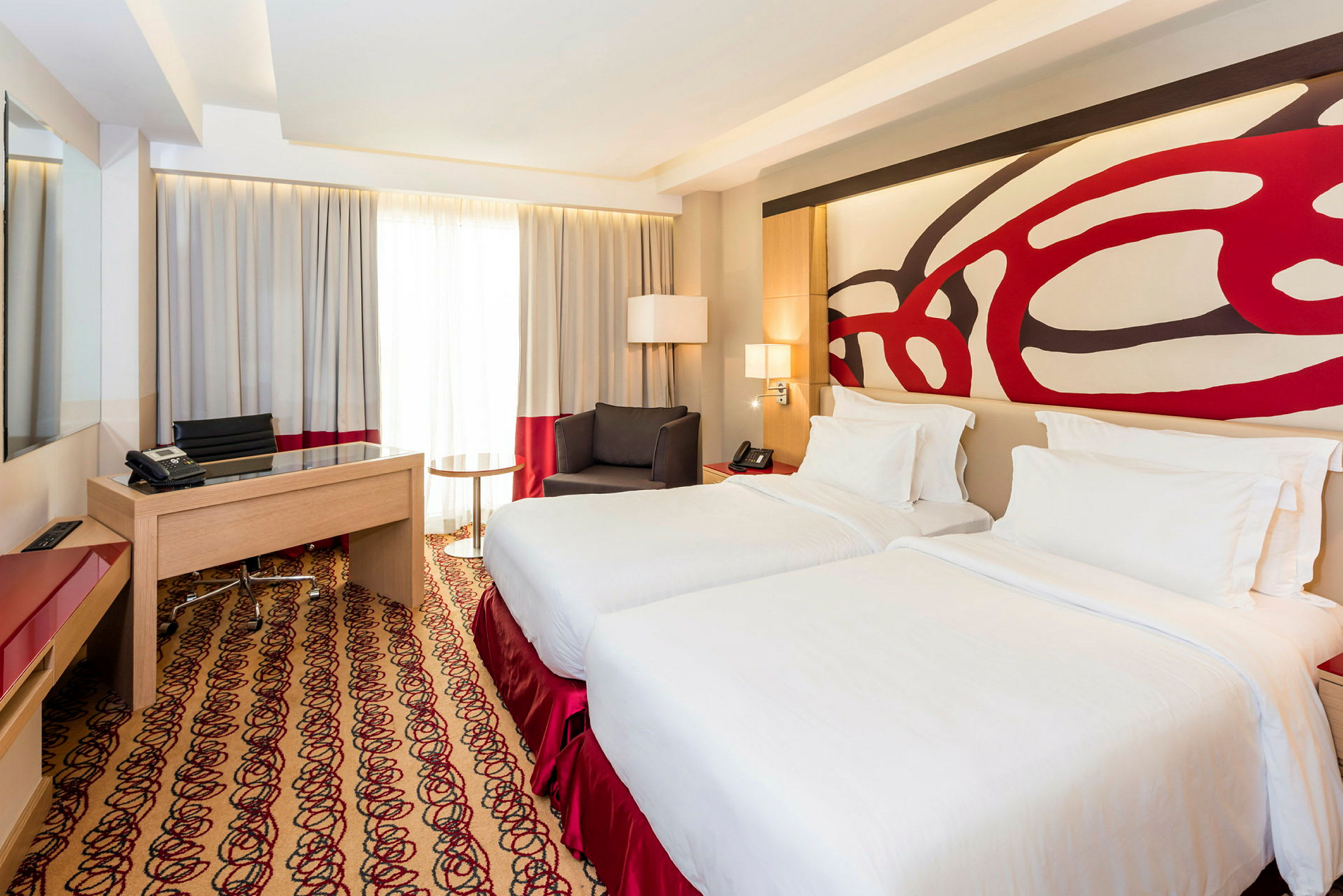 Ett hotellrum med två enkelsängar, ett skrivbord, en stol och ett fönster med gardiner. (AI-genererad text)