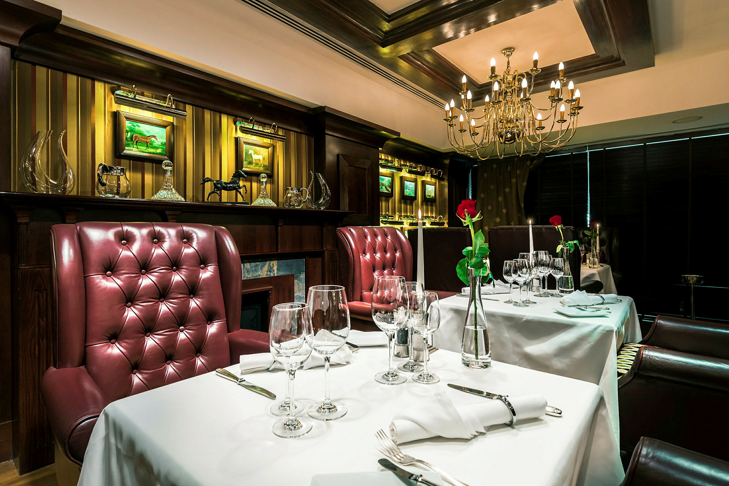 En elegant restaurangmiljö med bord klädda med vita dukar, röda stoppade stolar och ljuskrona i taket. (AI-genererad text)