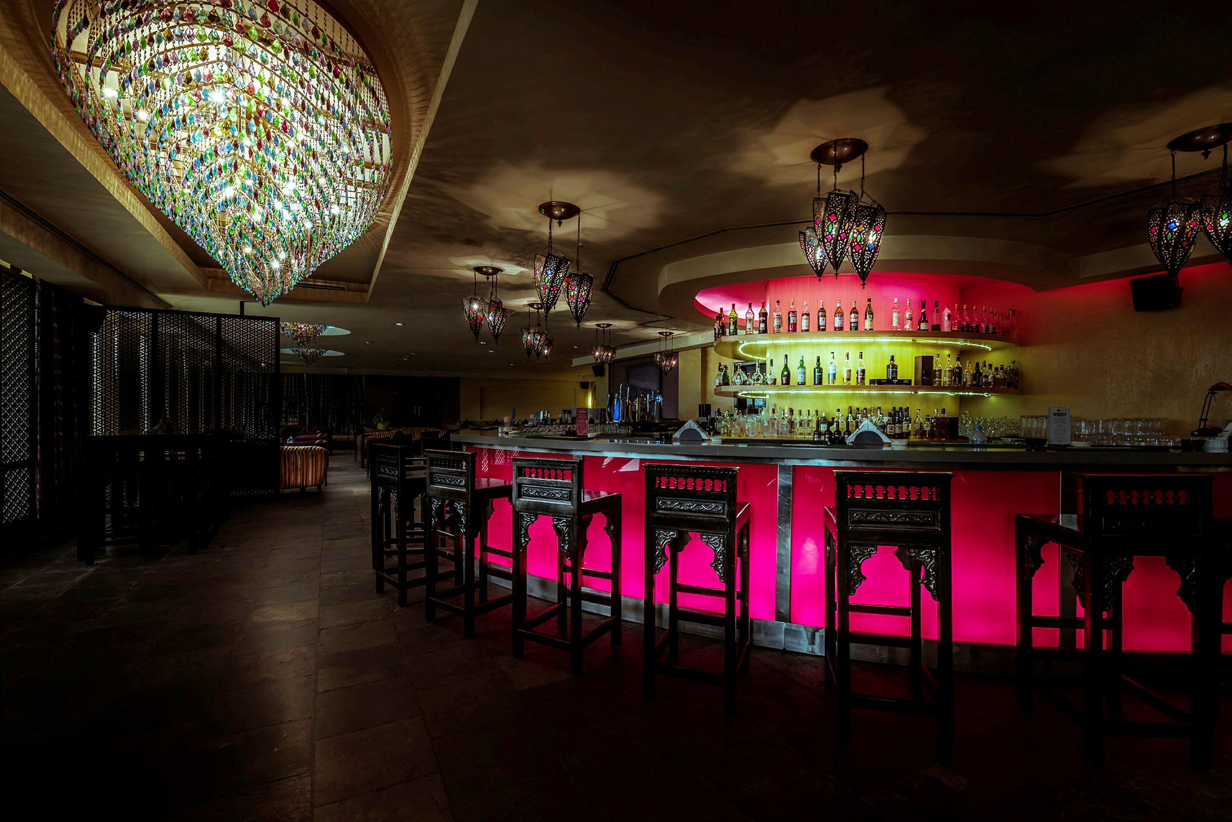 En elegant bar med upplyst bardisk i färgstarka toner och kristallkronor som hänger från taket. (AI-genererad text)
