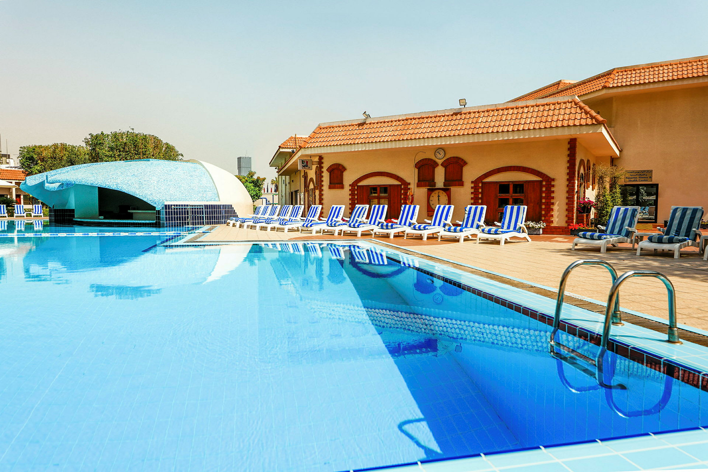 En pool vid ett hotell med solstolar och en bar i bakgrunden. (AI-genererad text)