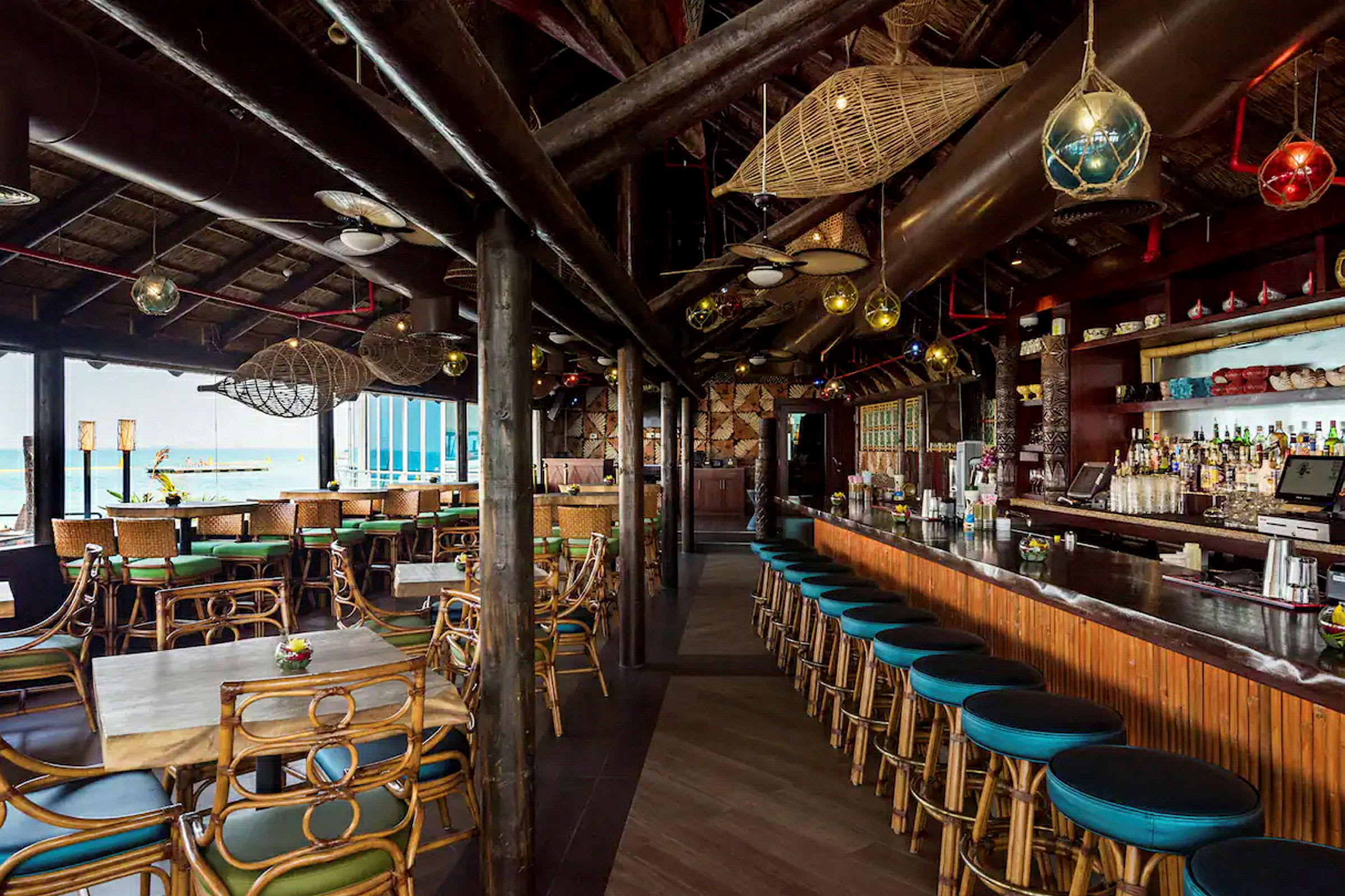 En interiör av en strandbar med rustik inredning, bambustolar och ett stort träbart deskrum. (AI-genererad text)
