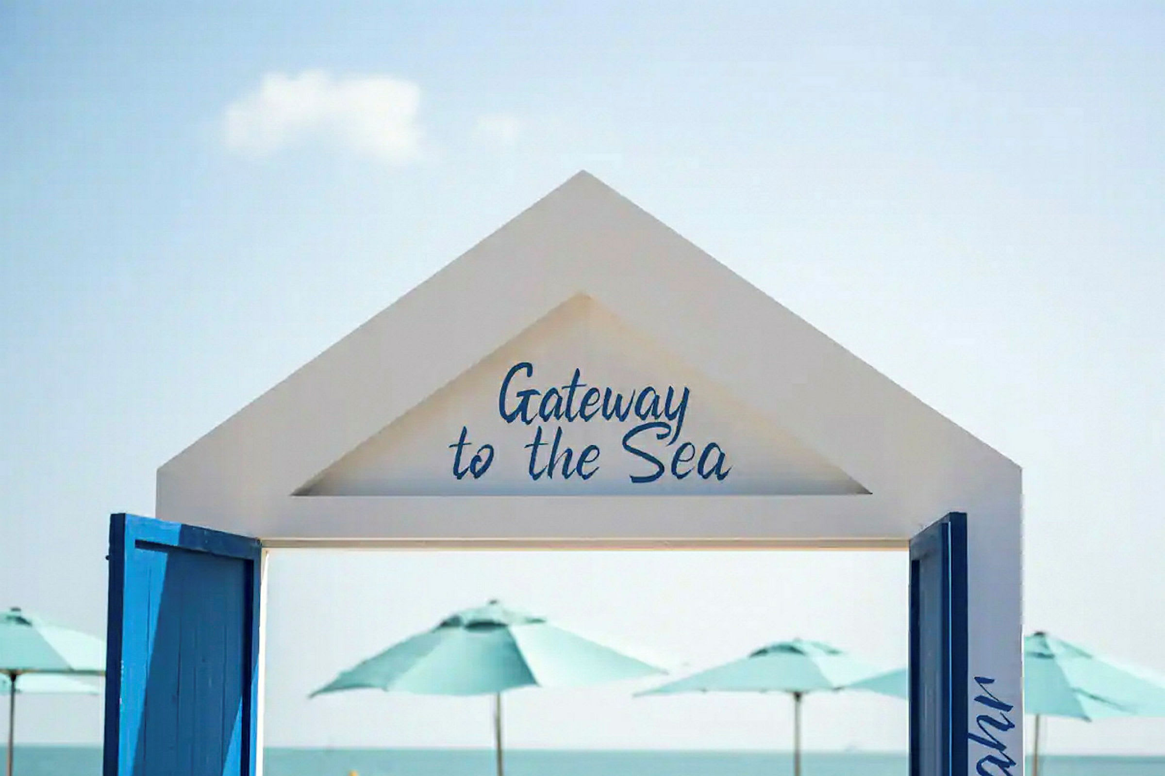 En vit portal med texten "Gateway to the Sea" med utsikt över havet och parasoller i bakgrunden. (AI-genererad text)