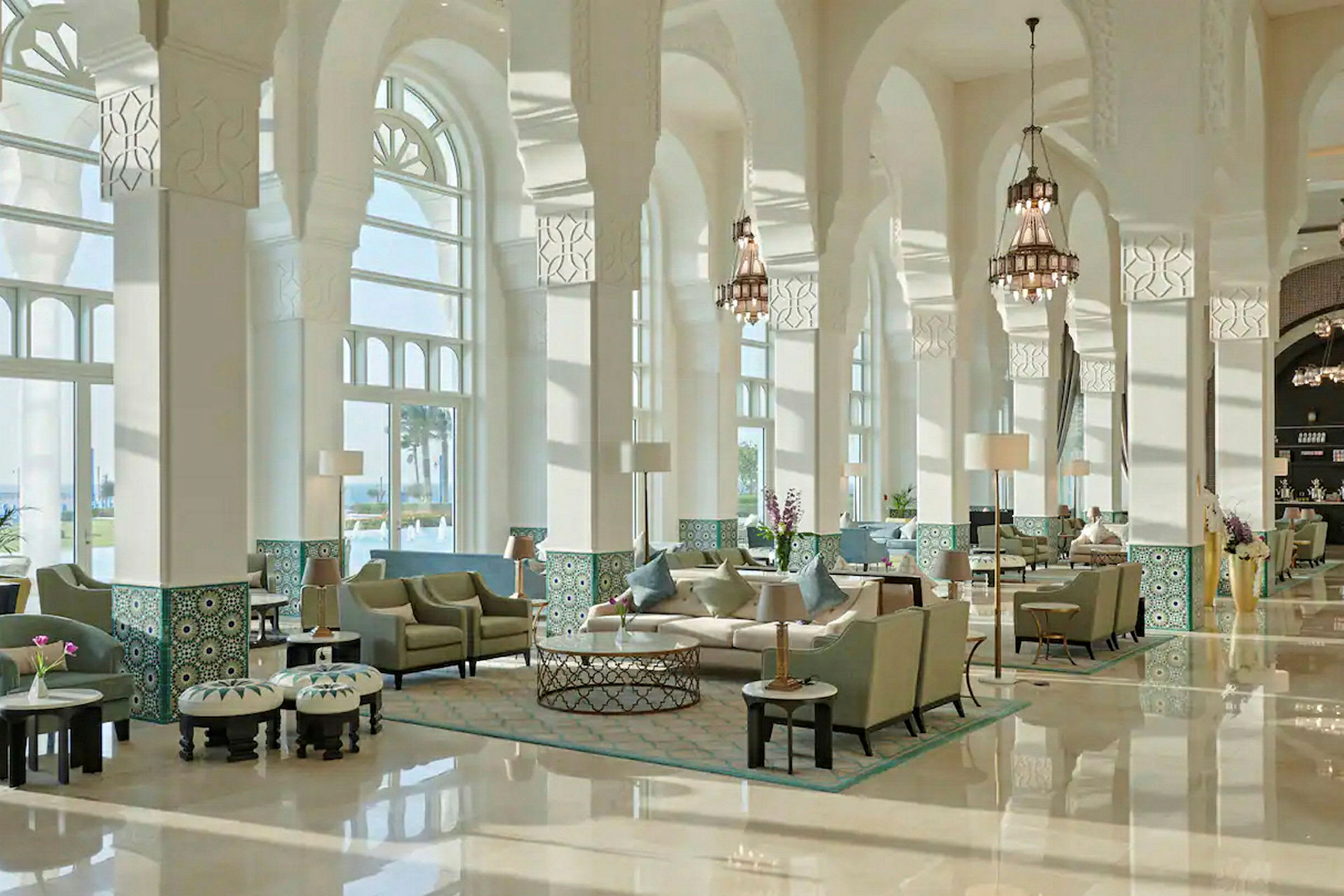 Ett elegant hotellobby med möblerade sittgrupper, höga välvda fönster och dekorativa pelare. (AI-genererad text)