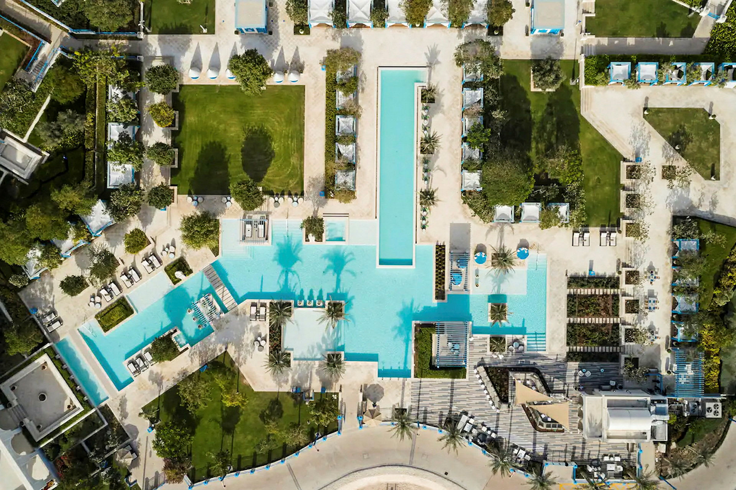 Flygvy över en pool på ett semesterresort omgivet av solstolar, grönytor och träd. (AI-genererad text)