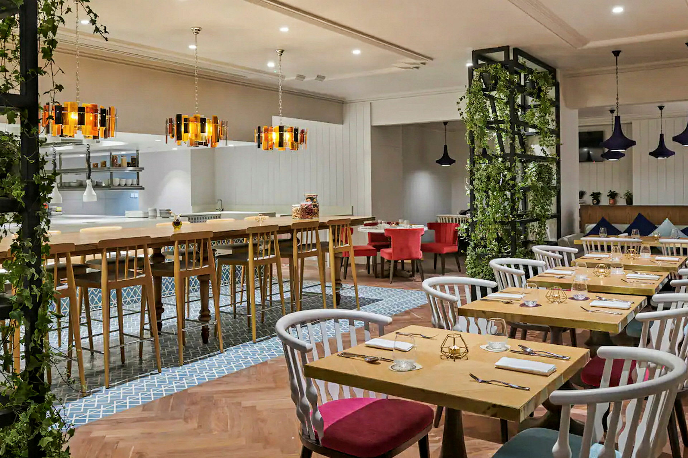 Bild av en restaurang med ett modernt inrett matområde, bord och stolar i olika färger samt dekorativa lampor. (AI-genererad text)