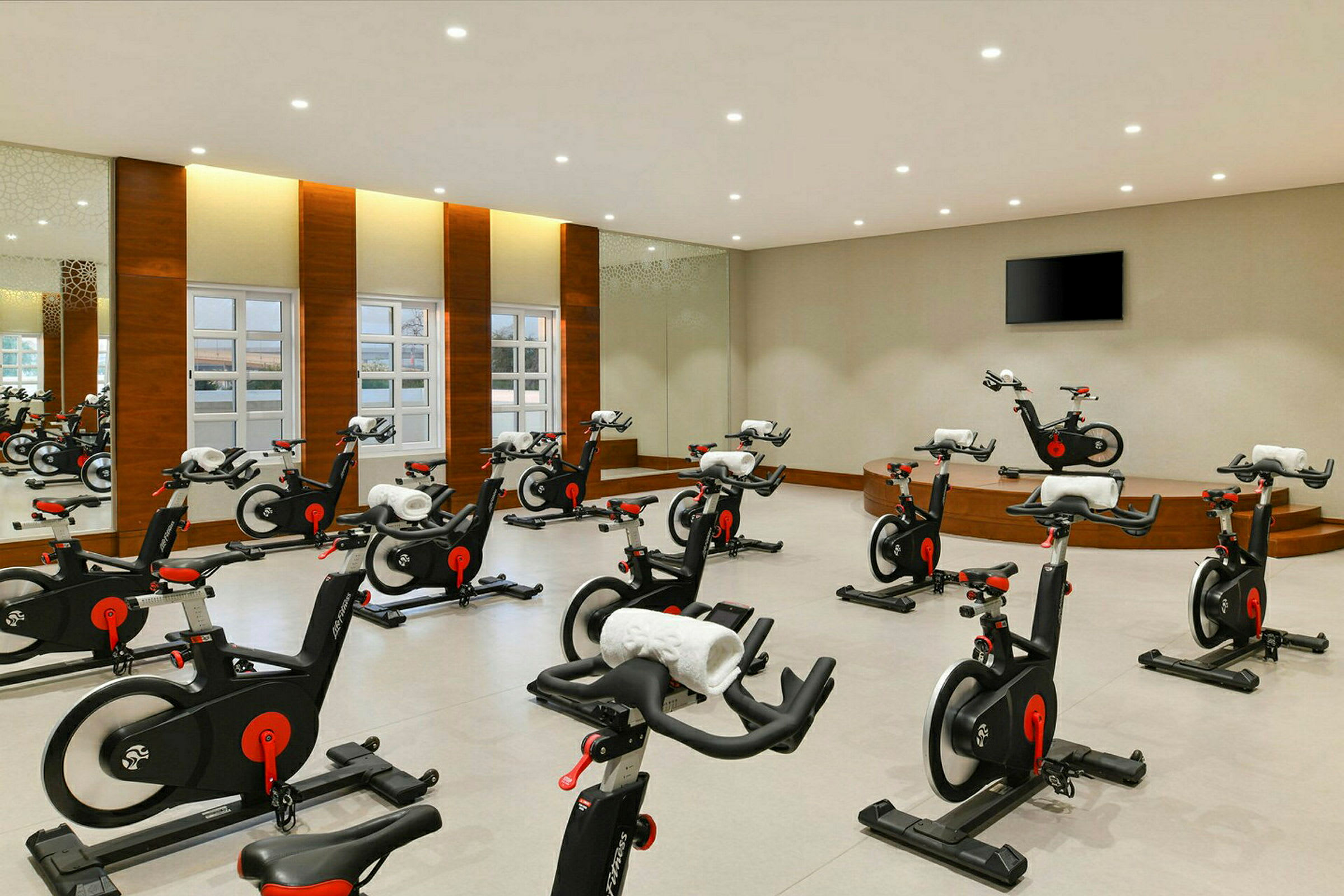 Ett gym med flera träningscyklar på rad i ett stort rum med speglar och fönster. (AI-genererad text)
